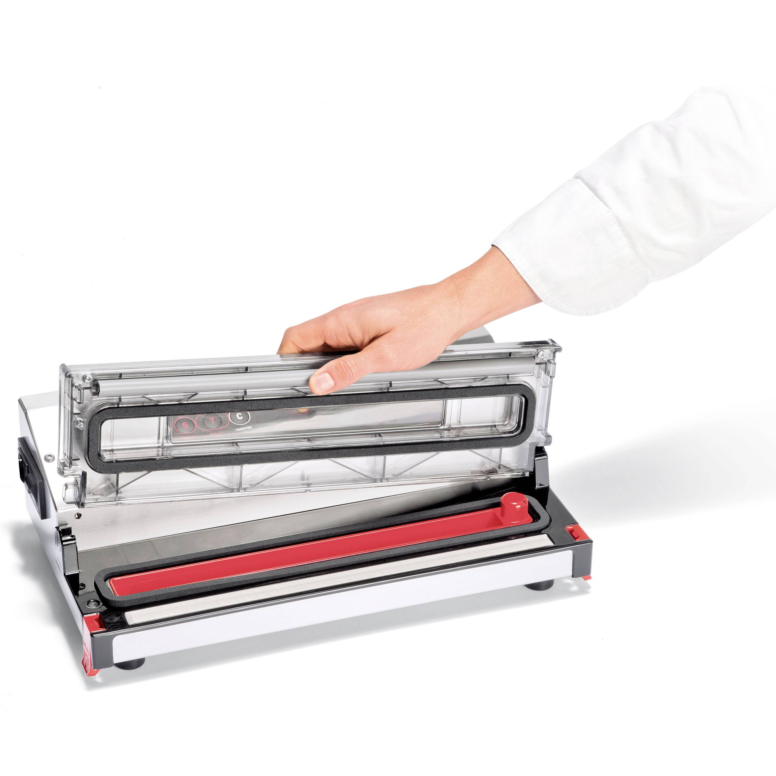 Ręka otwiera przezroczystą pokrywę urządzenia do pakowania próżniowego, które leży na białej powierzchni.