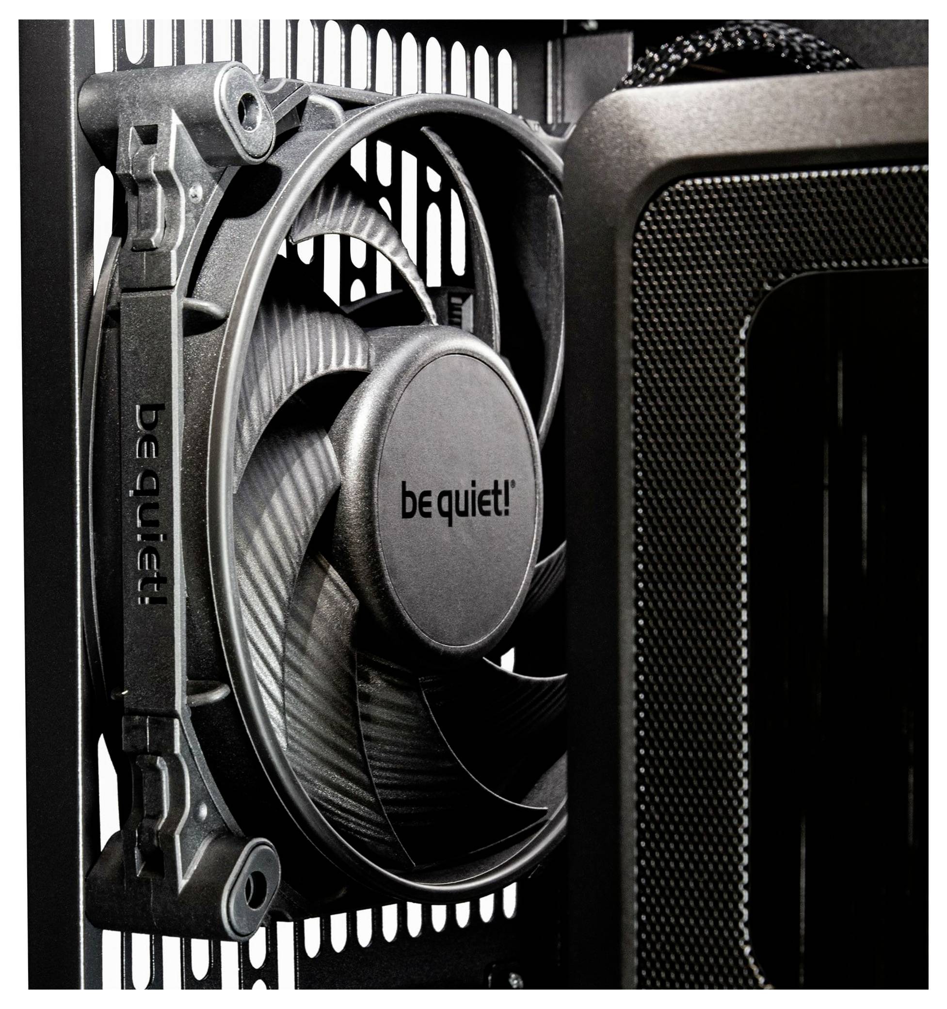 Zbliżenie wentylatora komputerowego z napisem 'be quiet!' zamontowanego w obudowie. Wentylator jest skierowany w lewo i podkreśla funkcję chłodzenia.