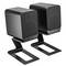 Dwa czarne głośniki na metalowych stojakach, stojące na płaskiej powierzchni. Projekt jest nowoczesny i minimalistyczny.