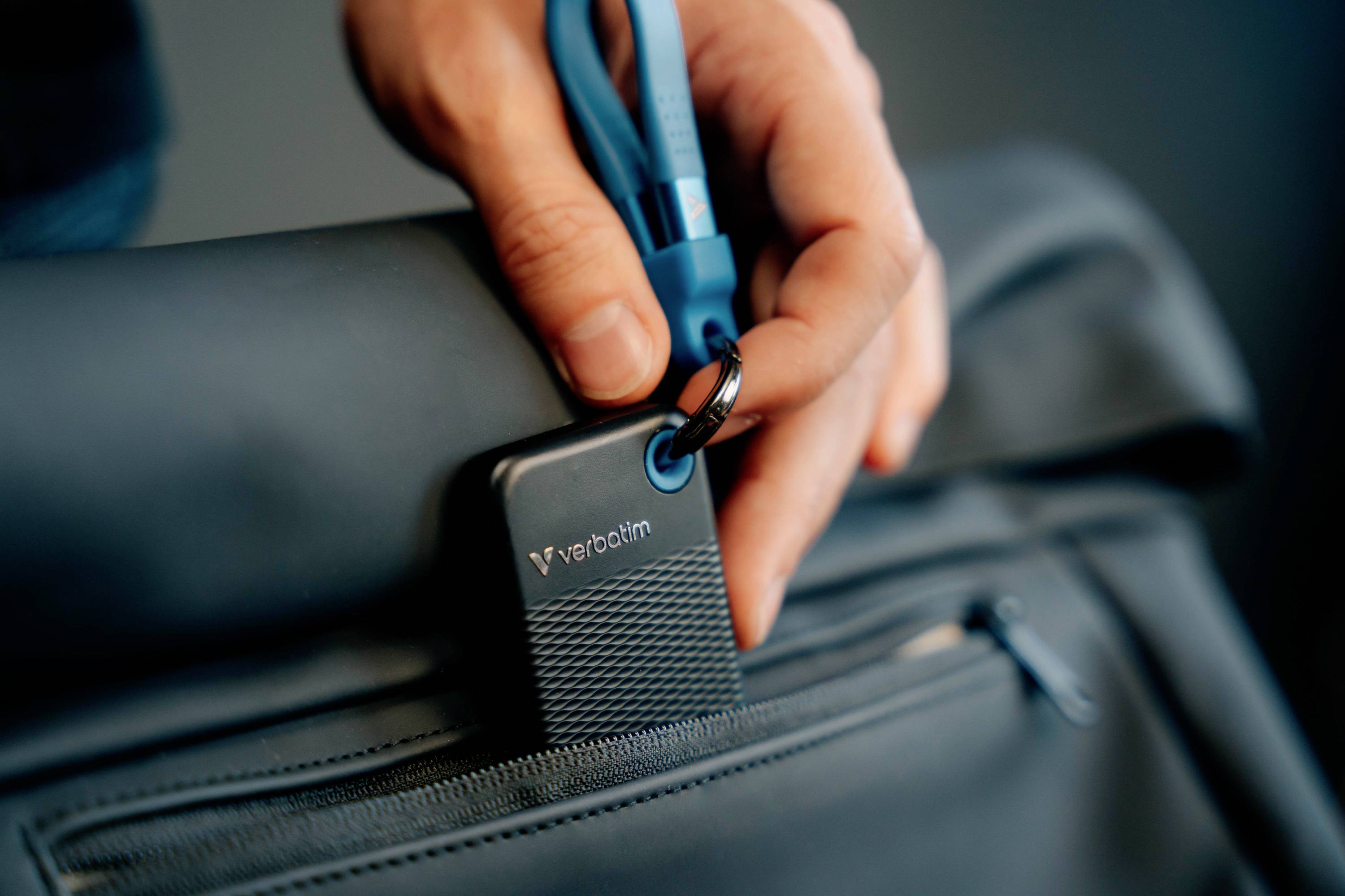 Ręka mocuje przenośny dysk SSD niebieskim kablem do czarnego plecaka.