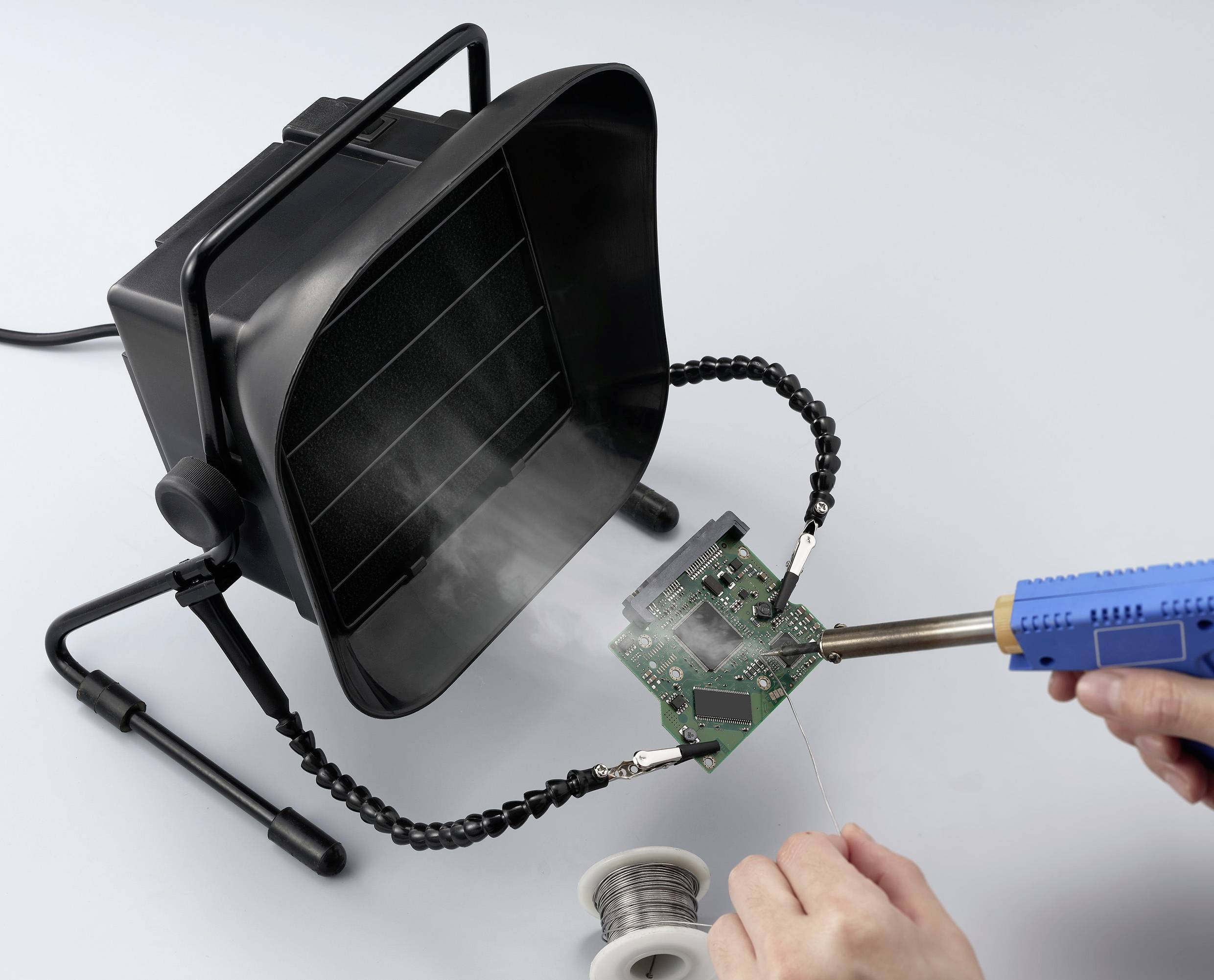 Osoba lutuje płytkę drukowaną za pomocą lutu, podczas gdy pochłaniacz dymu usuwa opary. W tle widać rolkę cyny lutowniczej.