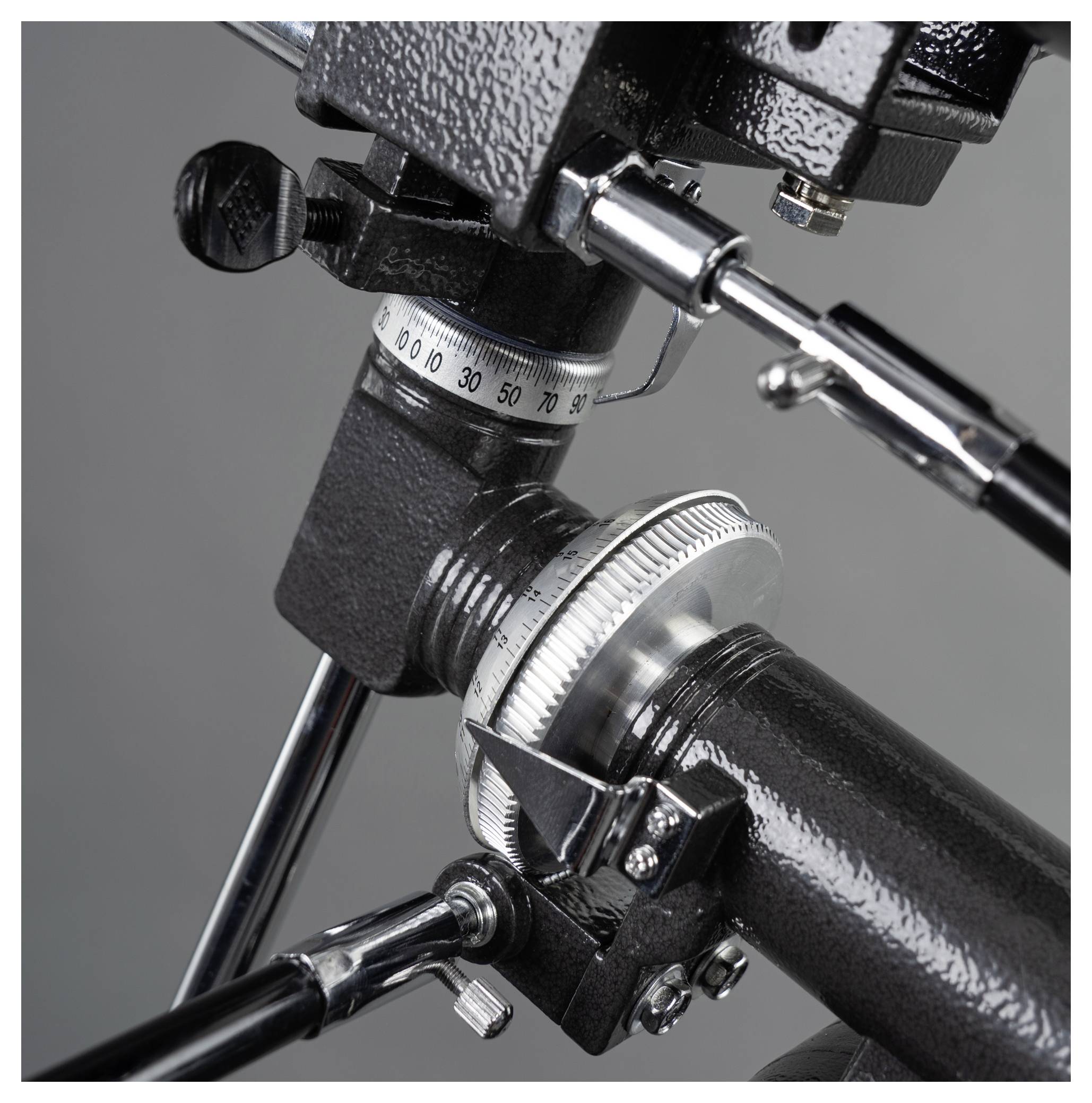 Zbliżenie głowicy statywowej wykonanej z metalu z naniesioną skalą, używanej do precyzyjnego ustawiania aparatów fotograficznych. Tło szare.