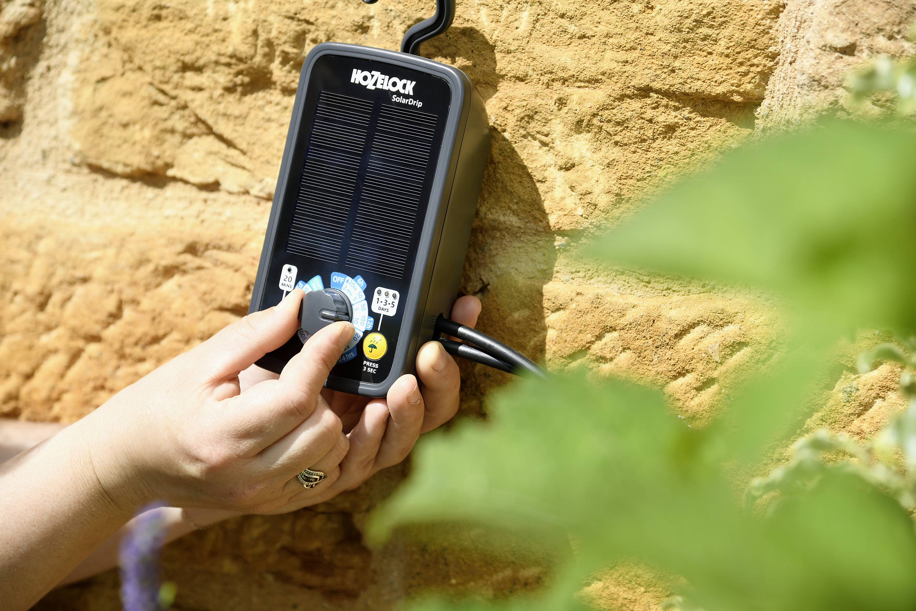 Osoba obsługuje system nawadniania na ścianie, regulując kąt rozproszenia strumienia. Na pierwszym planie widoczne są rośliny.