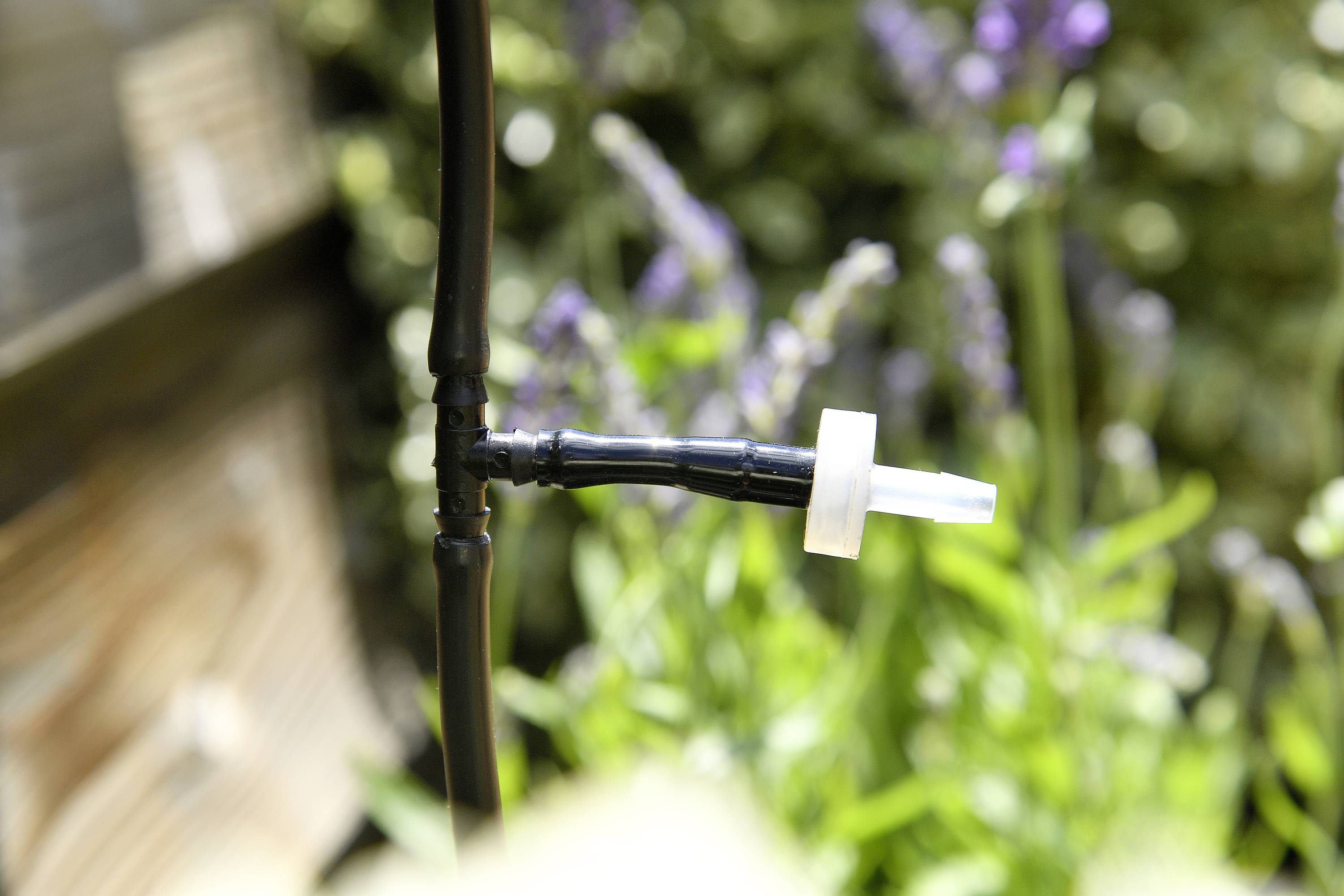 Zbliżenie złączki trójnikowej na wężu ogrodowym na niewyraźnym tle zielonych roślin i drewna.