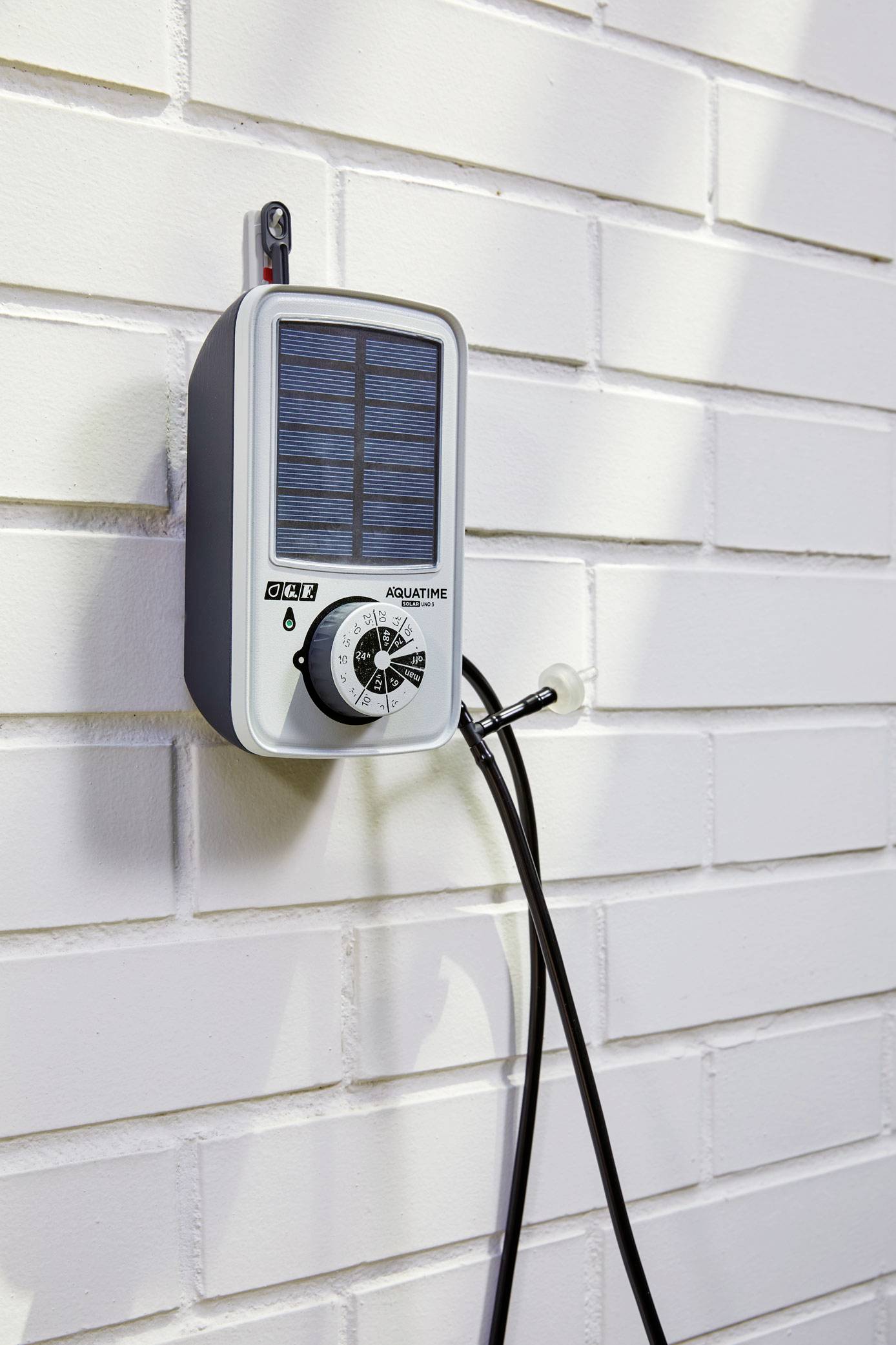 Urządzenie sterujące nawadnianiem zasilane energią słoneczną jest zamontowane na białej ścianie z cegły. Podłączony jest wąż wodny.