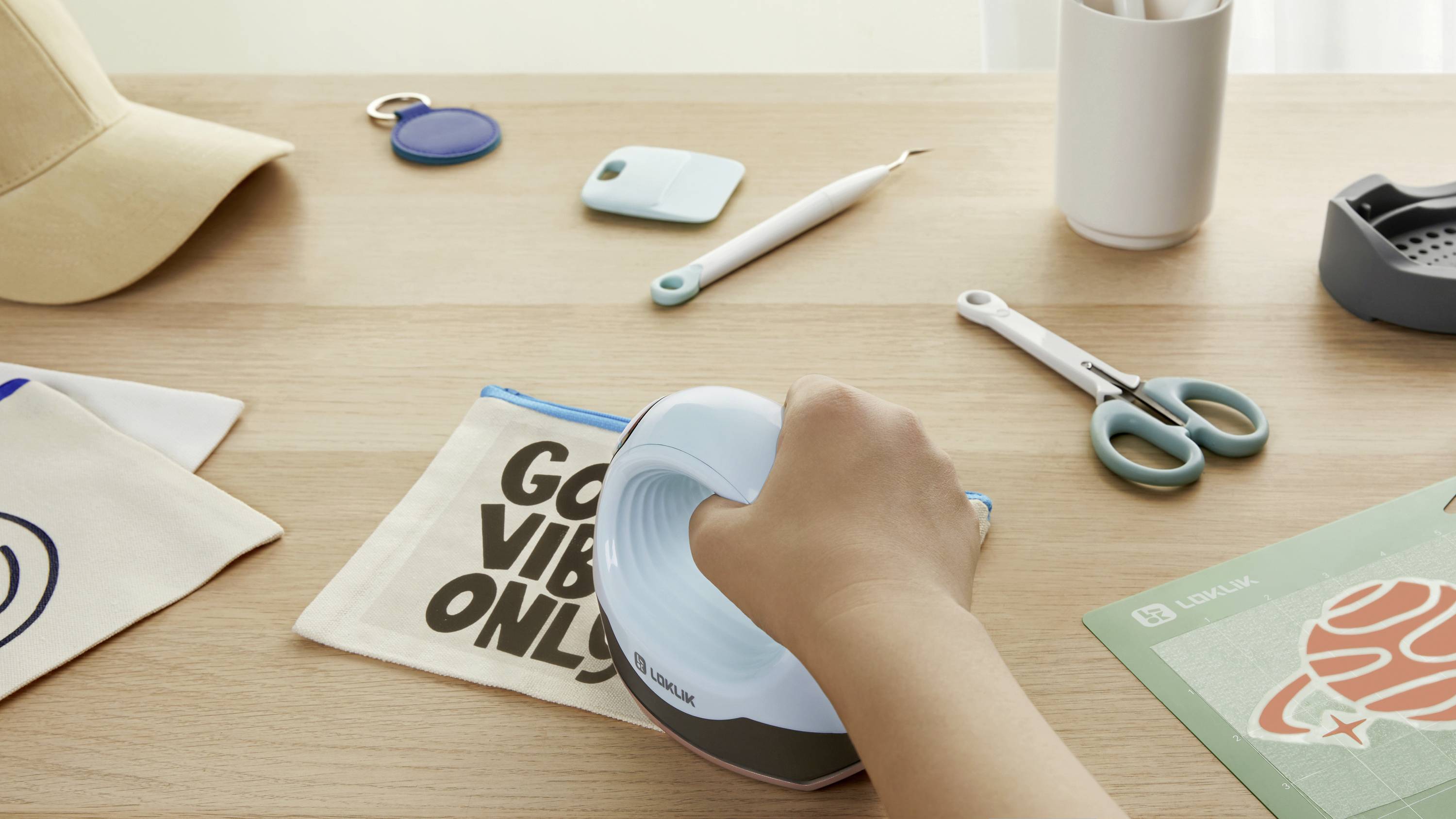 Osoba używa urządzenia do drukowania etykiet na stole, w tle widoczne są nożyczki, etui, długopis i inne przedmioty.