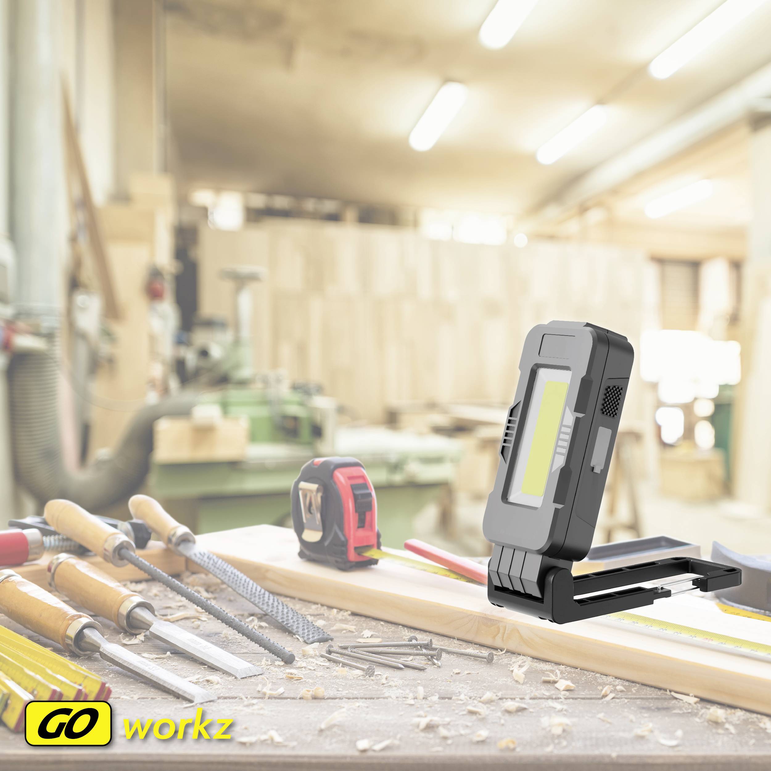 'Różne narzędzia i lampa na stole warsztatowym w dobrze oświetlonym warsztacie. W tle nieostre maszyny.'