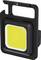 Kompaktowa, czarna przenośna lampa z jasnym, żółtym światłem LED pośrodku. Idealna do aktywności na świeżym powietrzu lub do użytku warsztatowego.