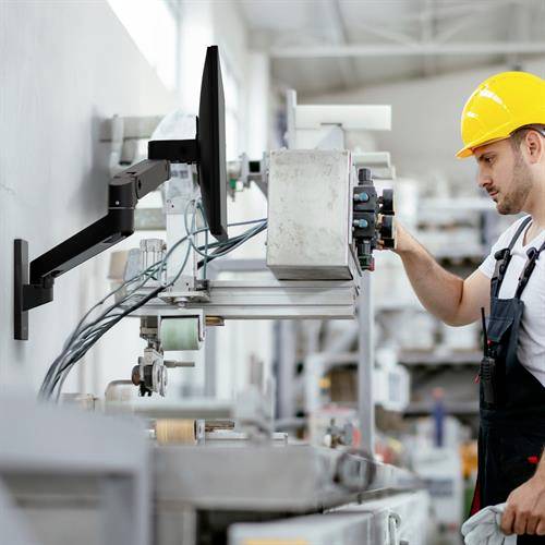 Mężczyzna w żółtym kasku ochronnym kontroluje maszyny w środowisku przemysłowym.