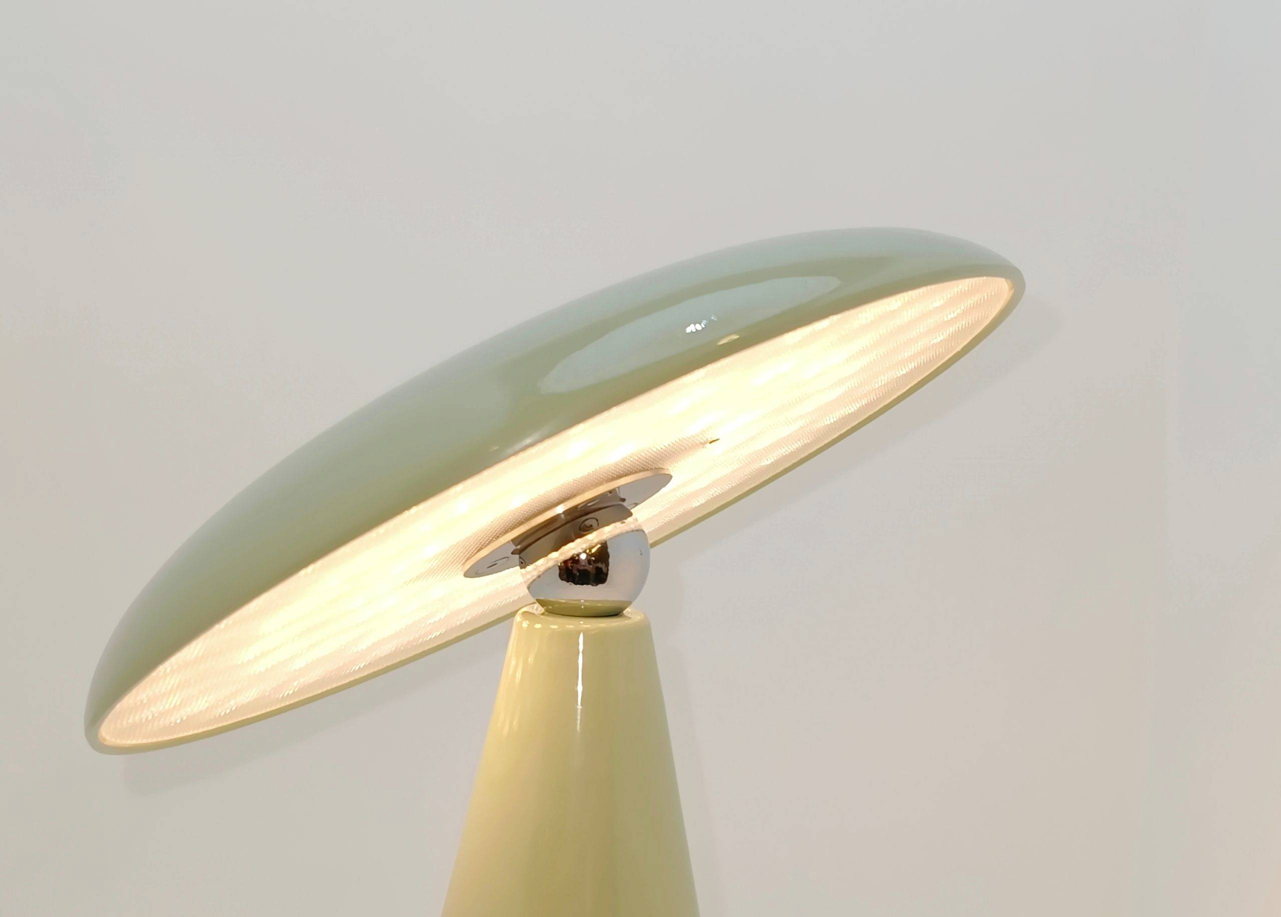 Stylowa lampa stołowa z lśniącym, owalnym kloszem metalowym, która roztacza ciepłe światło, spoczywająca na smukłej podstawie.