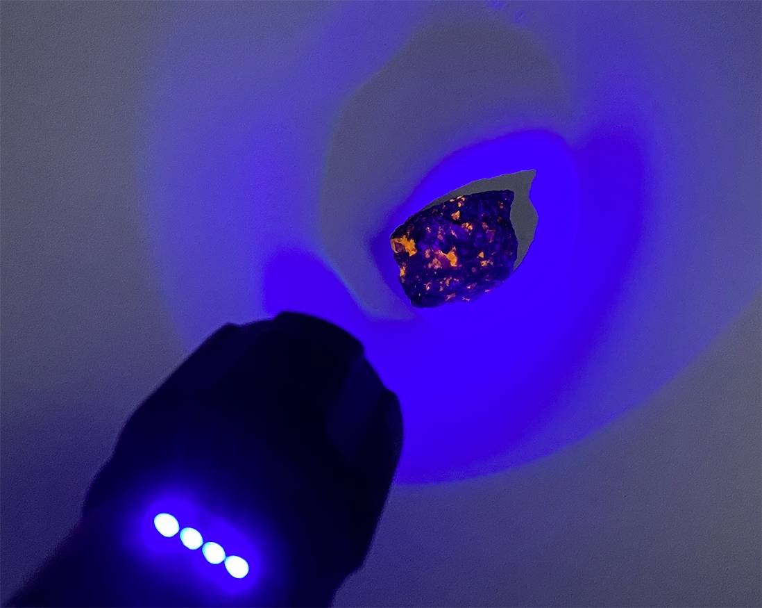 Niebieskie źródło światła oświetla ciemny kamień, powodując widoczne pomarańczowe refleksy.