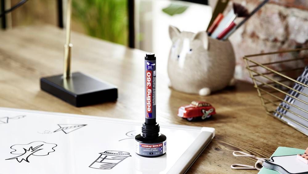 Tablica whiteboard na biurku, na której widoczne są szkice. Obok leży marker edding 360 i uchwyt na długopisy w kształcie kota.