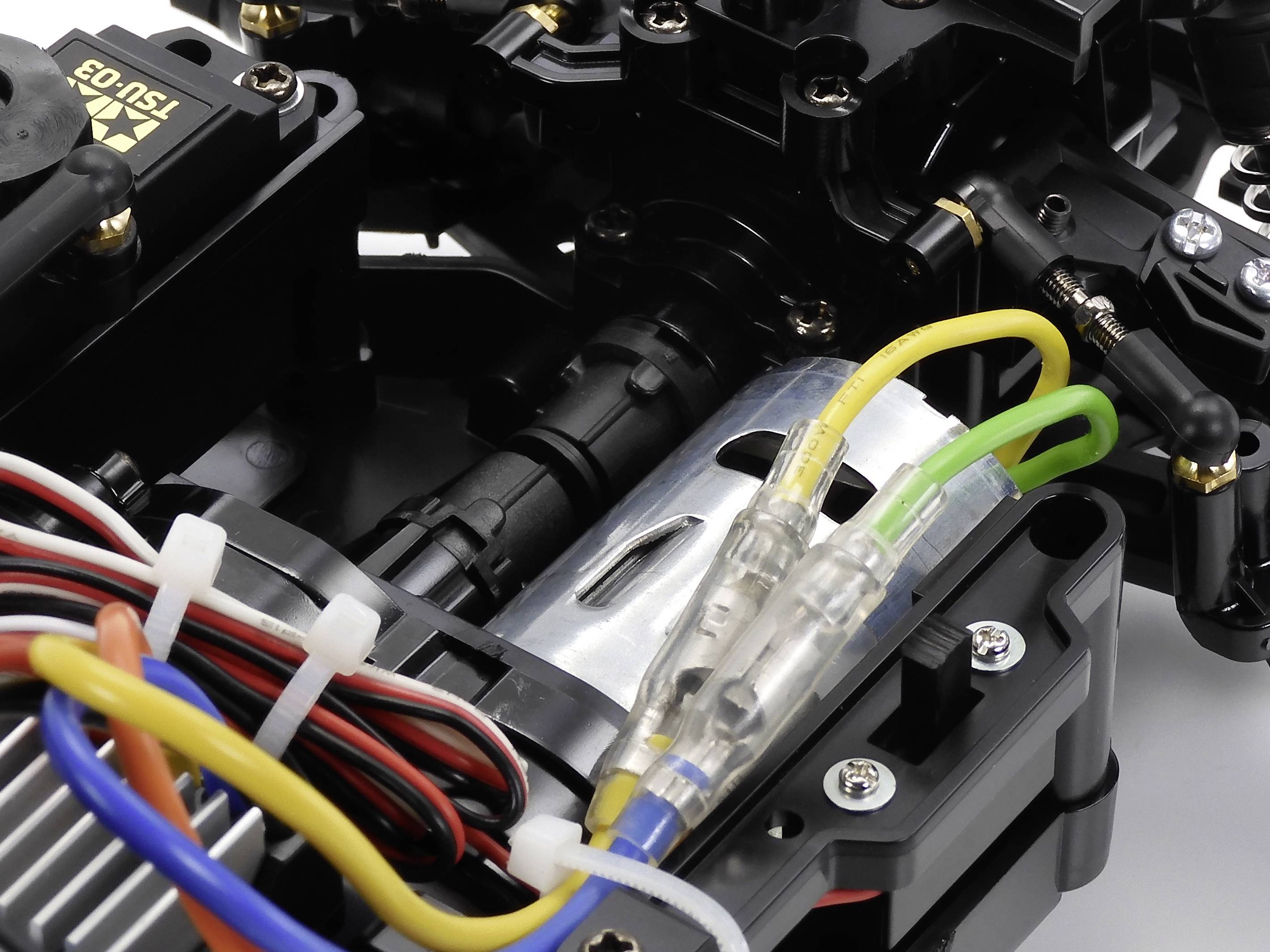 Zbliżenie podwozia samochodu zdalnie sterowanego z widocznymi kolorowymi przewodami i elementami mechanicznymi.