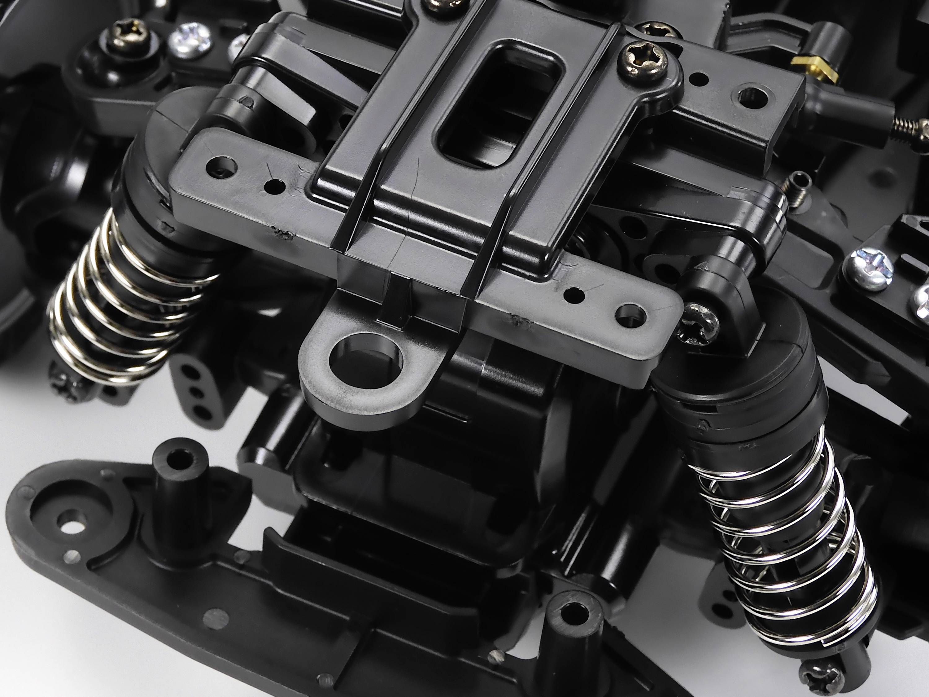 Zbliżenie czarnego elementu mechanicznego z sprężynami i śrubami, prawdopodobnie fragment zawieszenia lub systemu silnikowego.