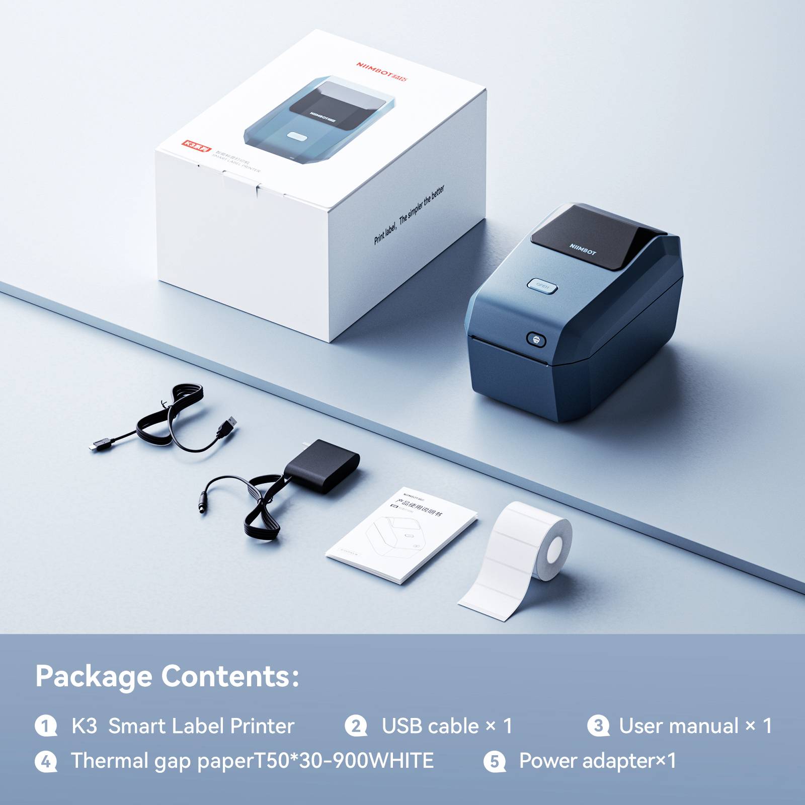 Drukarka etykiet K3 Smart Label stoi na stole, wyposażona w akcesoria: zasilacz, kabel USB, podręcznik użytkownika oraz rolkę papieru termicznego. W tle widoczne jest opakowanie.