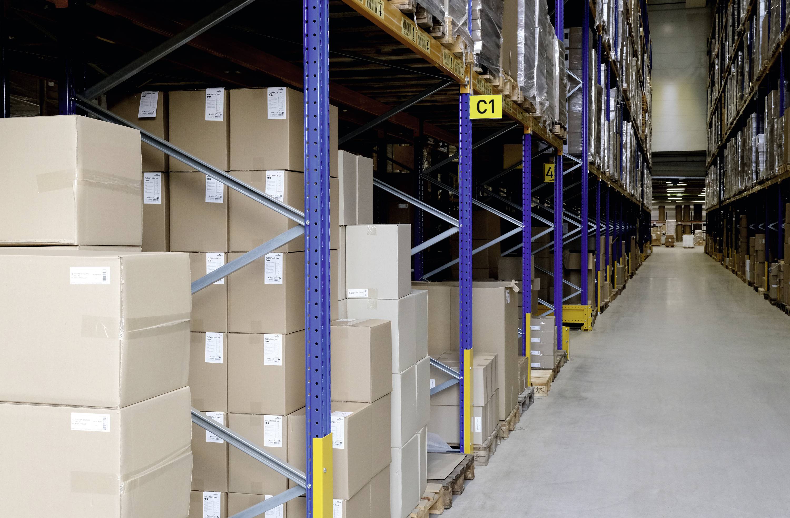 Magazyn z ułożonymi kartonami na regałach paletowych. Długi korytarz ciągnie się wzdłuż regałów sięgających aż do sufitu.