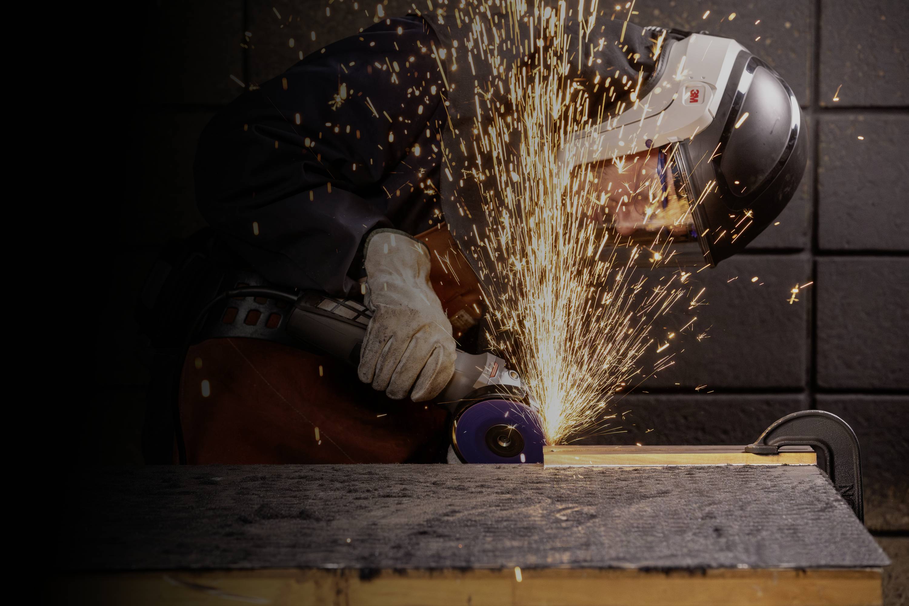 Osoba ubrana jest w odzież ochronną i używa szlifierki kątowej, podczas gdy dookoła lecą iskry.