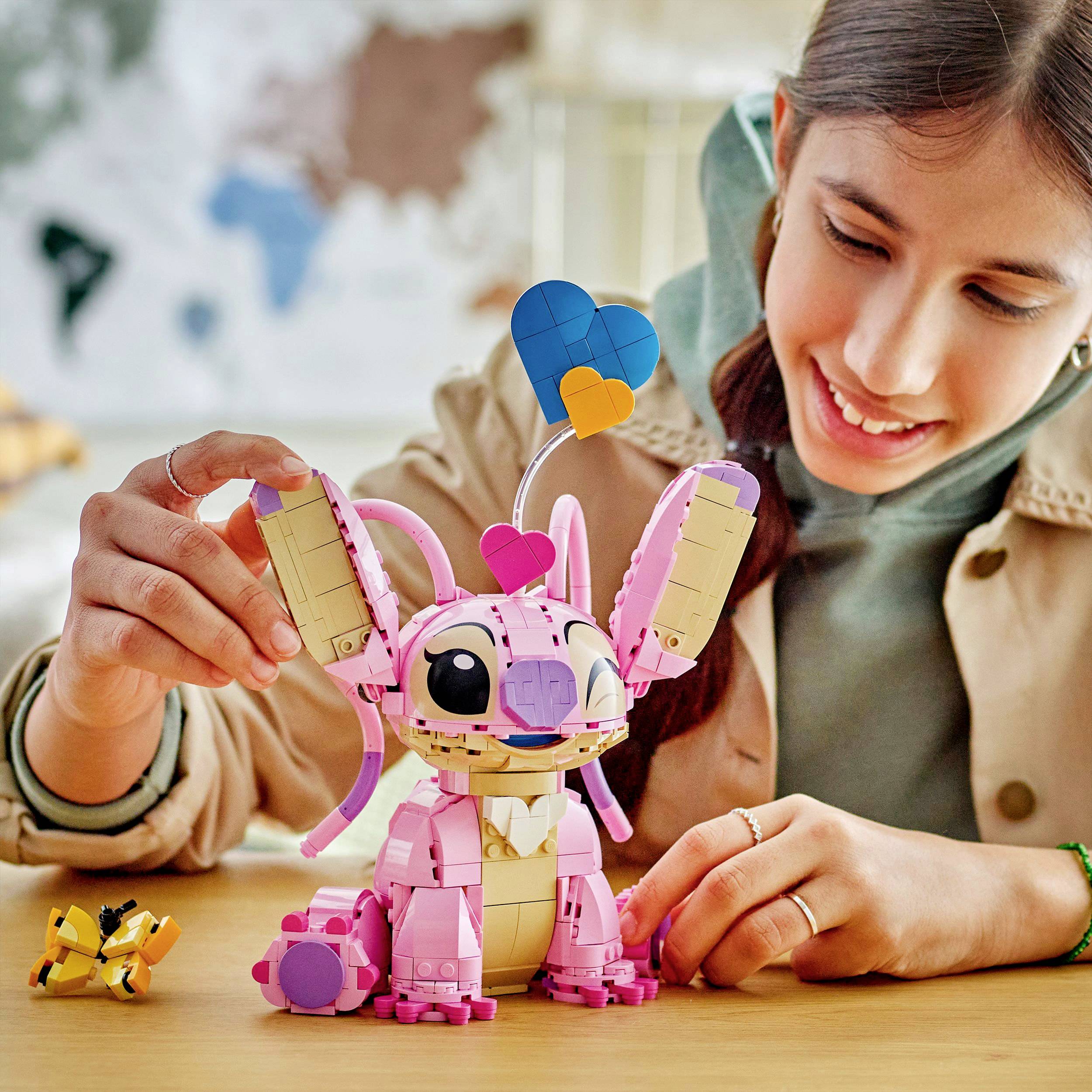 Śmiejąca się kobieta siedzi przy stole i bawi się różowym zabawkowym robotem, który ma kolorowe serduszka na głowie.