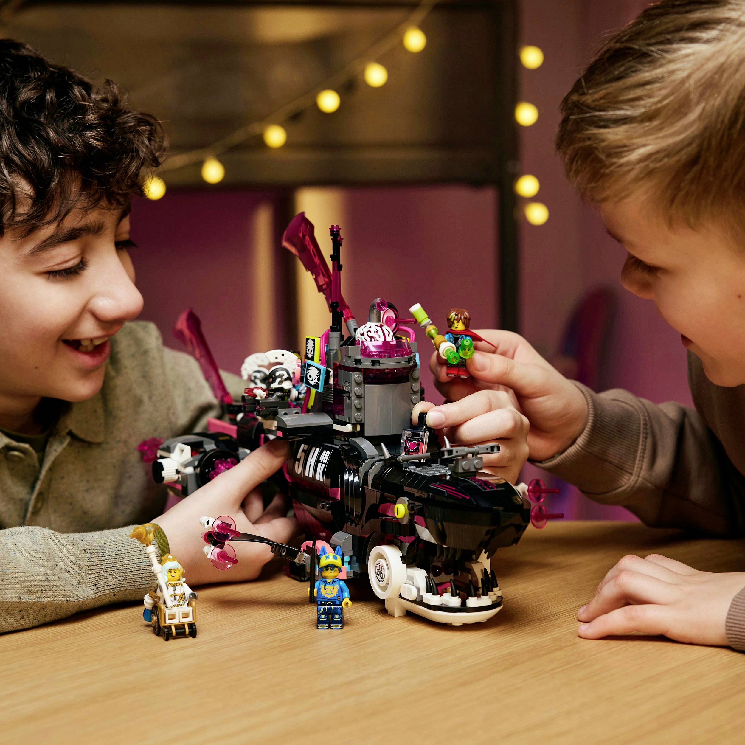 Dwoje dzieci bawi się radośnie kolorowym, szczegółowym zabawkowym statkiem kosmicznym na stole. W tle widać światła.