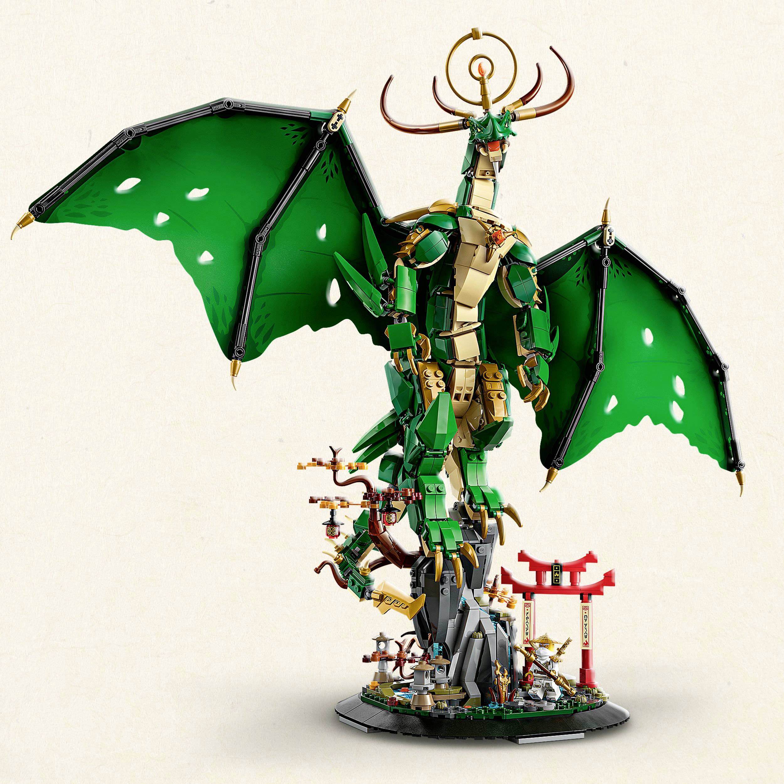 Duży, kunsztowny model zielonego smoka z rozpostartymi skrzydłami i złotymi detalami, stojący na skalnej podstawie z roślinami.