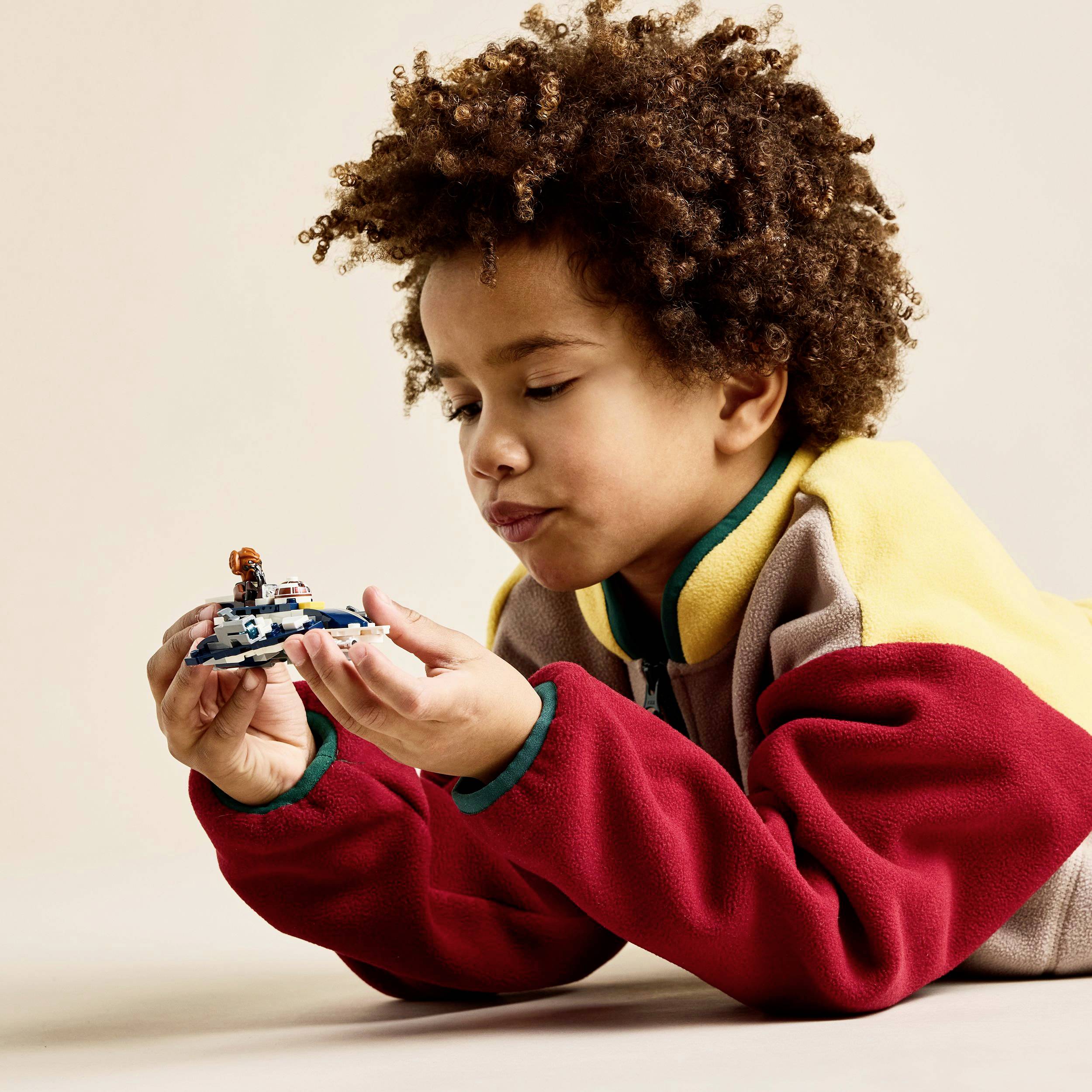 Dziecko z kręconymi włosami bawi się skupione małym zabawkowym statkiem kosmicznym i nosi kolorową kurtkę.