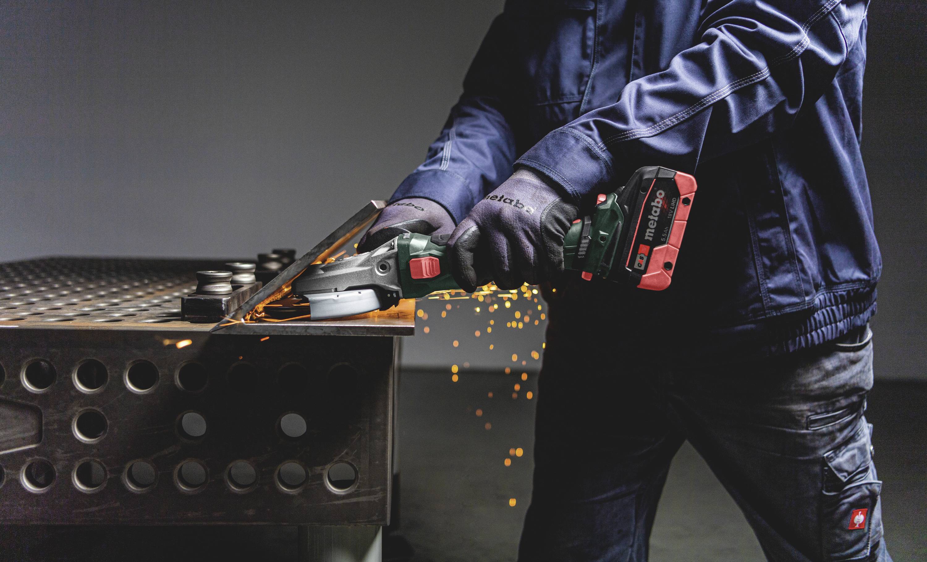 Osoba ucina metal kątówką, a wokół sypią się iskry. Zdjęcie koncentruje się na narzędziu i sytuacji roboczej.