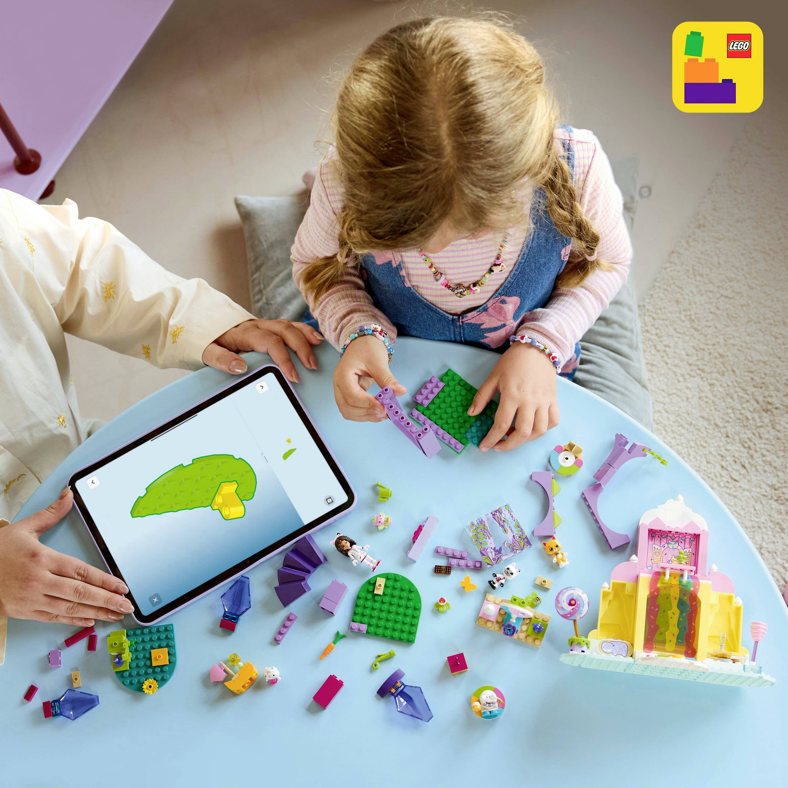 Dzieci bawiące się kolorowymi klockami LEGO, montujące strukturę przy użyciu cyfrowego tabletu wyświetlającego instrukcje montażu.