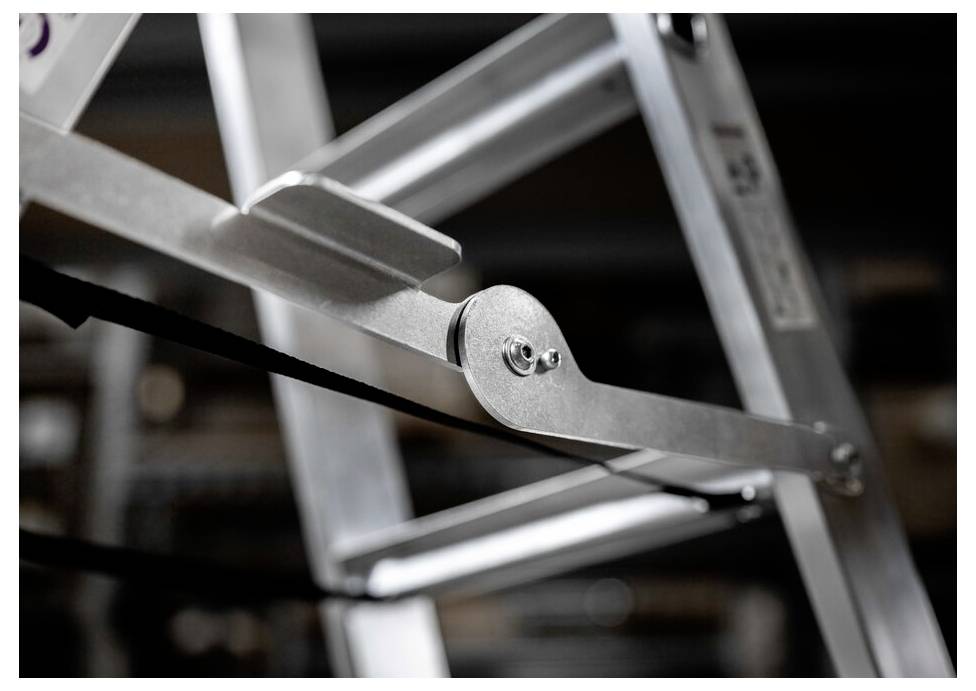 Zbliżenie drabiny aluminiowej sfotografowanej pod skosnym kątem z boku. Widoczne są szczegóły stopni i przegubów.