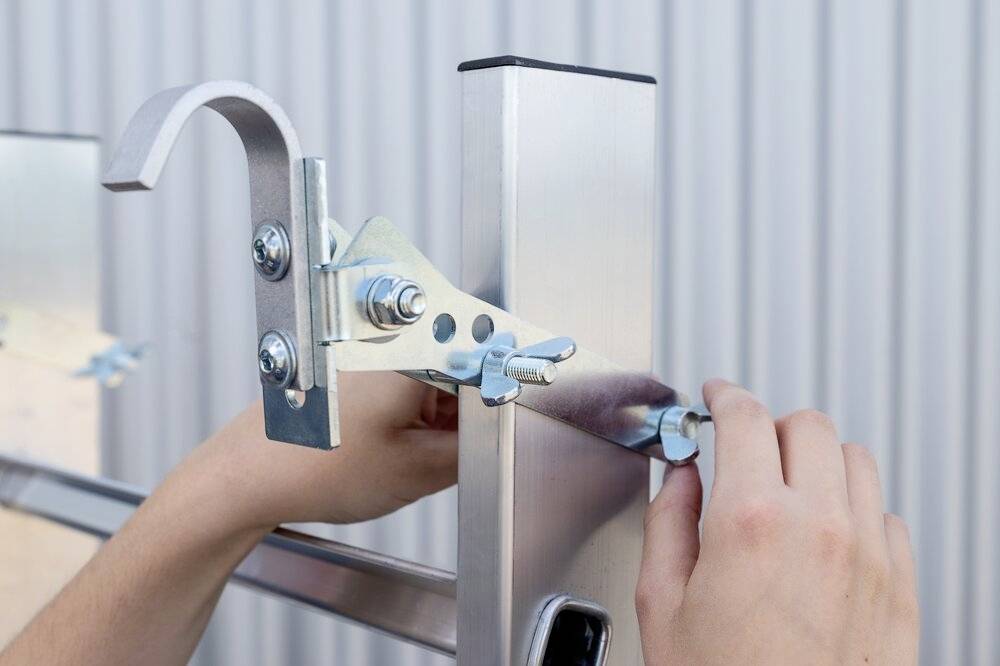Ręce regulują metalowy zacisk na pionowej aluminiowej ramie na tle w paski.