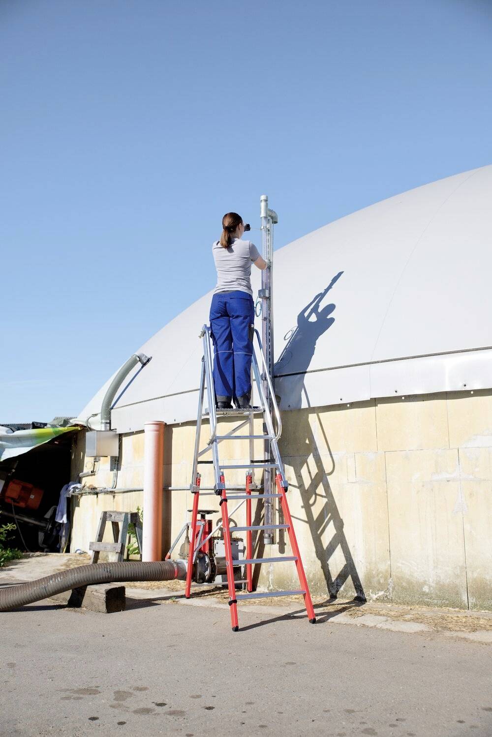 Kobieta stoi na drabinie i pracuje przy urządzeniu na dachu budynku. Jest to struktura w kształcie kuli.