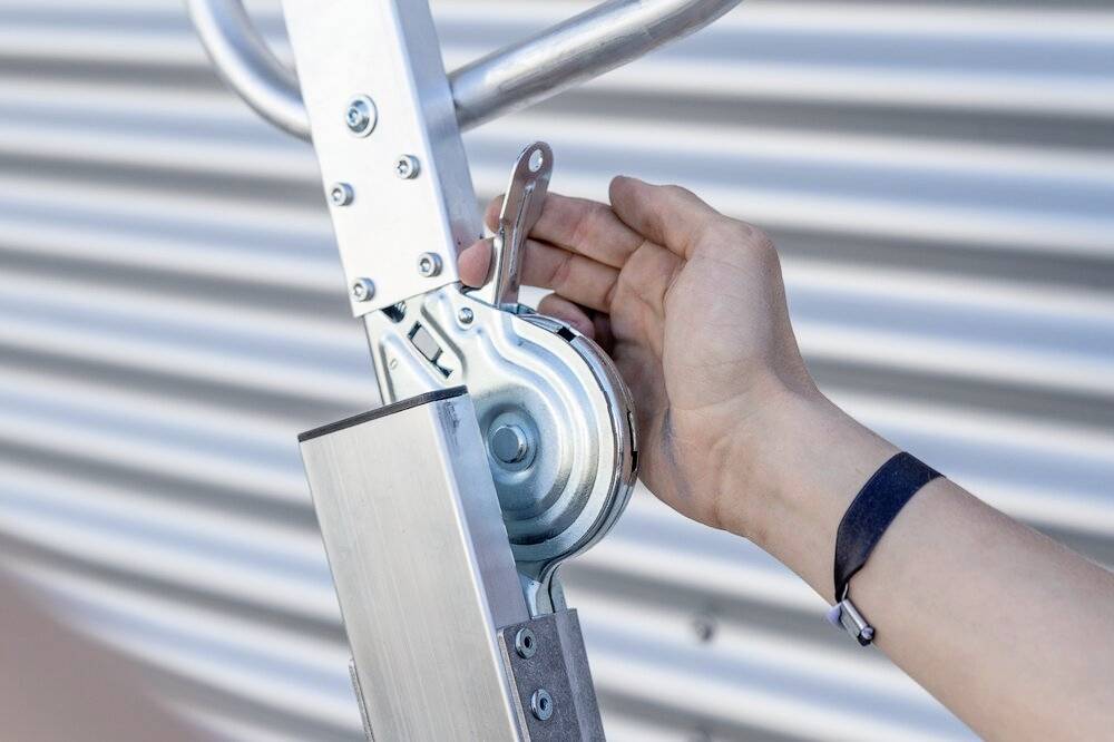 Ręka obraca mechaniczną korbą metalowego urządzenia na falistym tle.