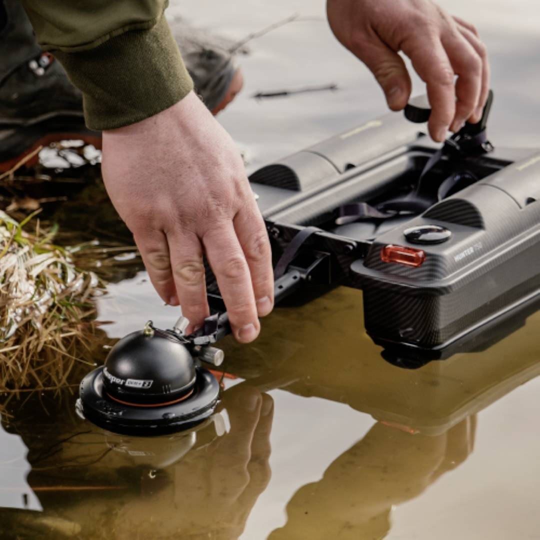 Osoba umieszcza czarną, zdalnie sterowaną łódź na wodzie. Wydaje się, że jest ona używana do celów badawczych lub rozpoznawczych.