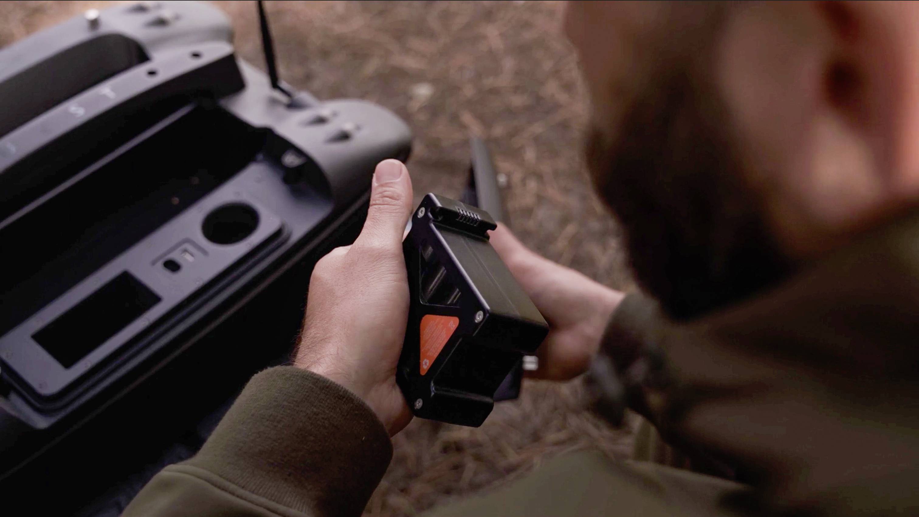 Osoba trzyma urządzenie techniczne z charakterystycznym czerwonym elementem; obok otwarta szuflada dużego, ciemnego urządzenia.