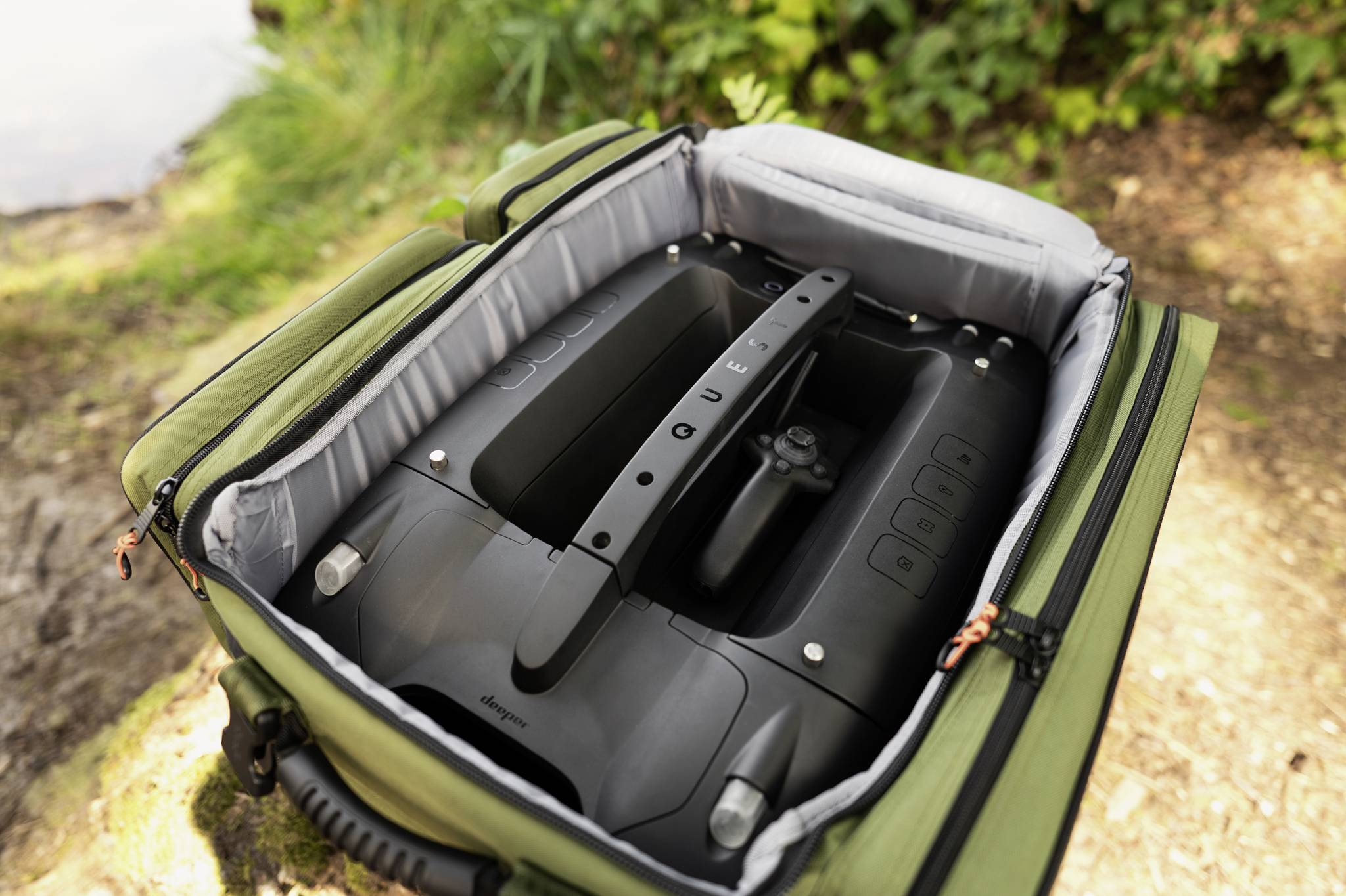 Przenośna maszyna bębnowa w otwartej, wyściełanej walizce, otoczona zielenią przyrody.