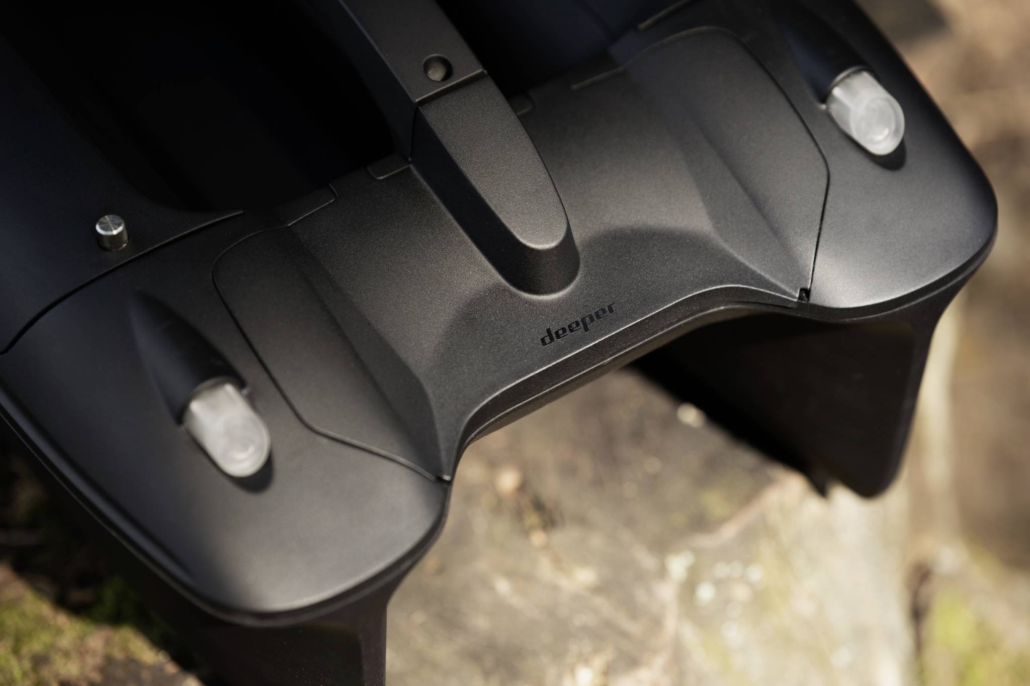 Czarne, opływowe urządzenie z dwoma okrągłymi sensorami leży na pniu ściętego drzewa. Otoczenie rozmyte, fokus na technologii.