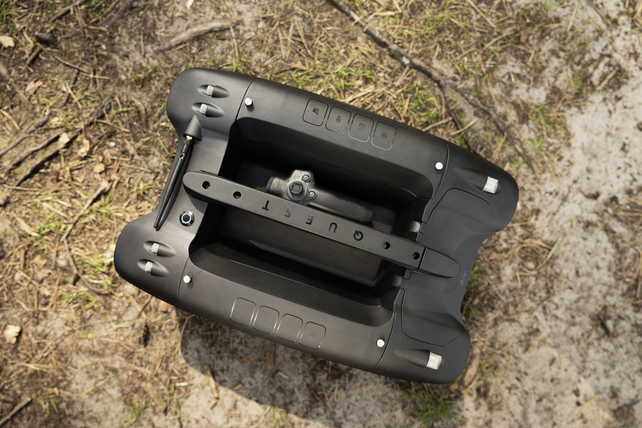 Nadzór drona: Czarny dron naziemny na ziemi z plamkami trawy. Dron posiada oznaczone przyciski na górnej powierzchni.