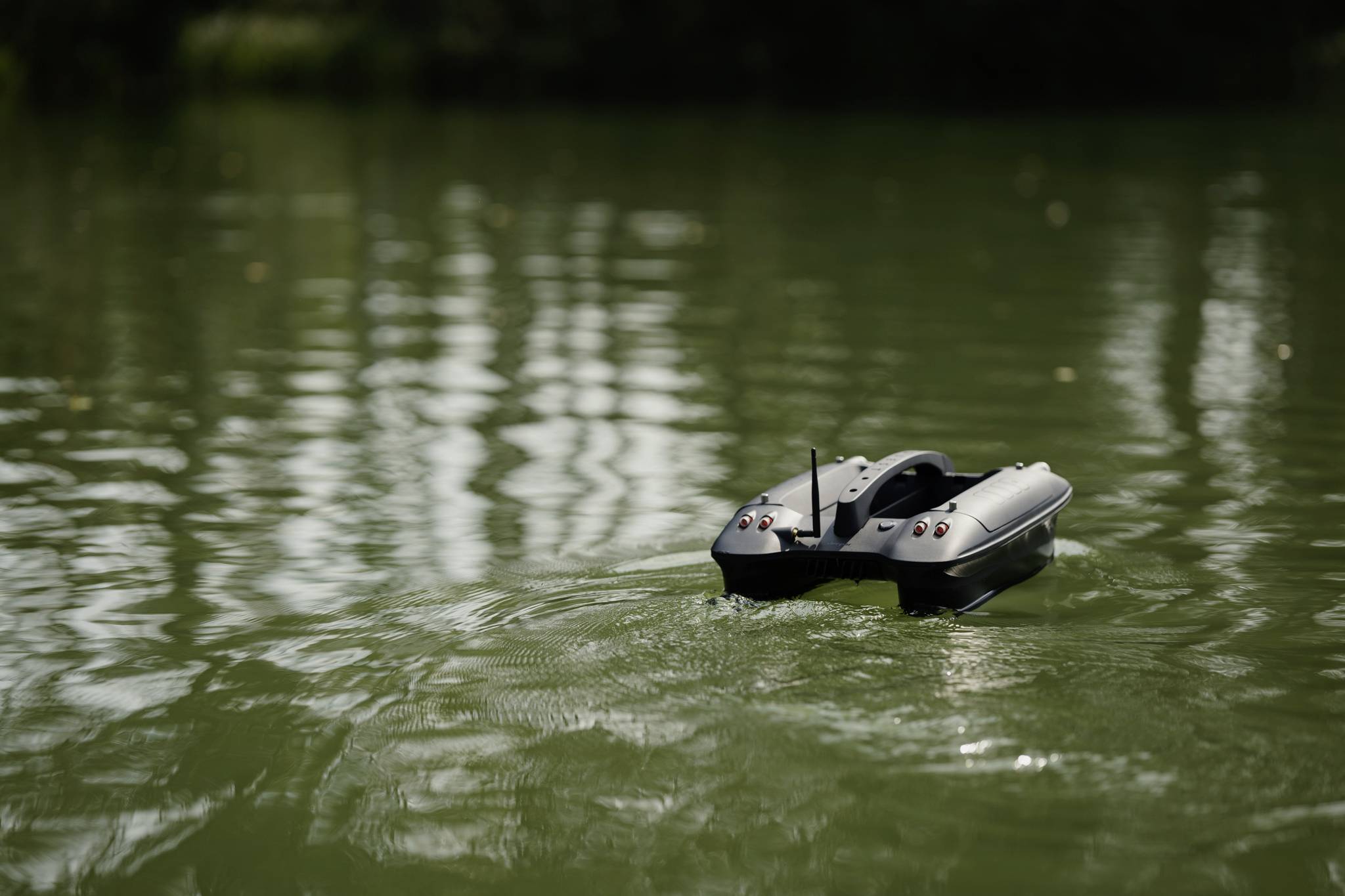 Zdalnie sterowana łódź pływa po spokojnym, zielonym jeziorze.