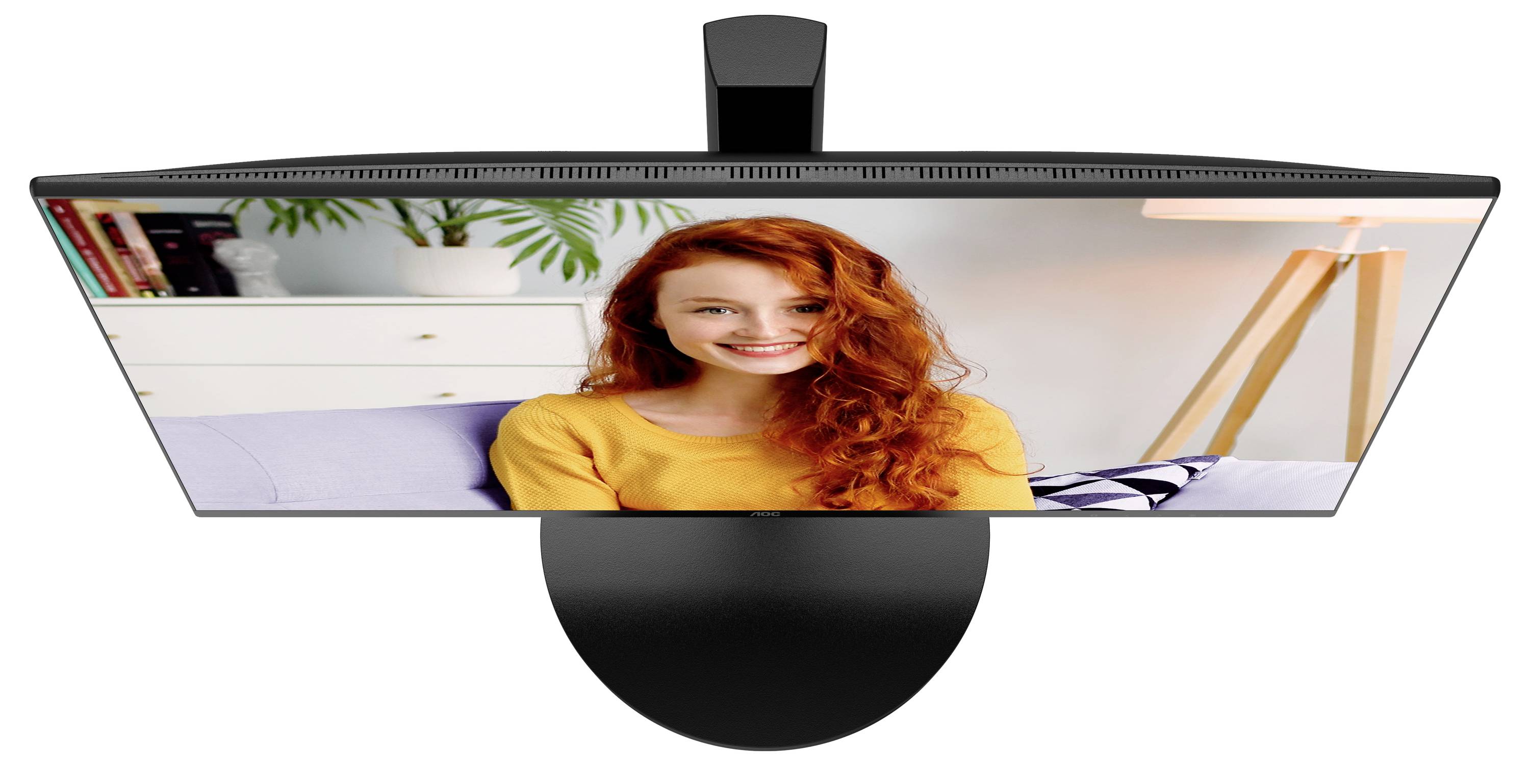 Osoba o rudych włosach uśmiecha się do kamery, siedząc na kanapie w nowocześnie urządzonym pomieszczeniu.