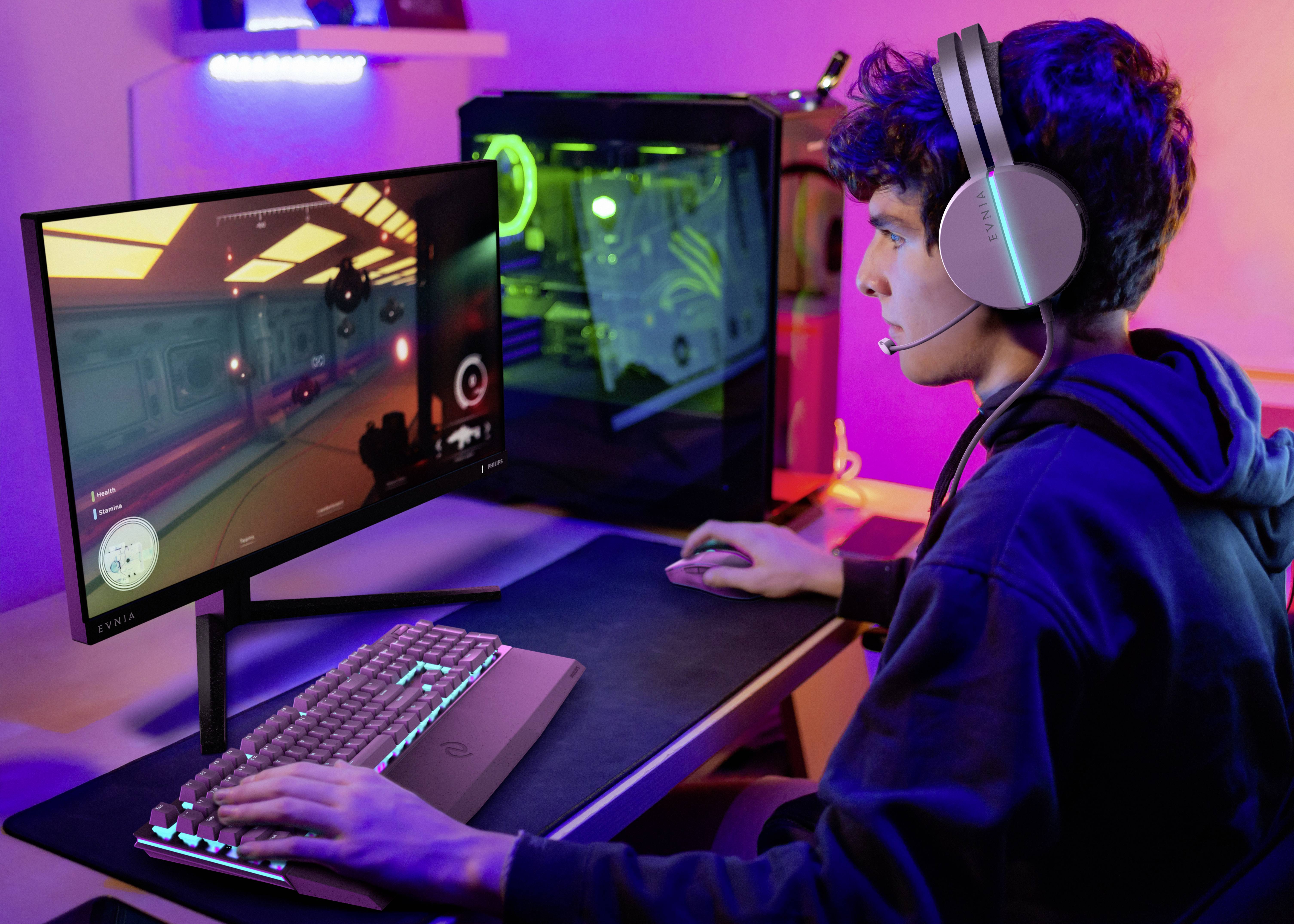 Młody mężczyzna siedzi przy biurku i gra w grę wideo na komputerze. Ma na głowie słuchawki i korzysta z klawiatury oraz myszy.