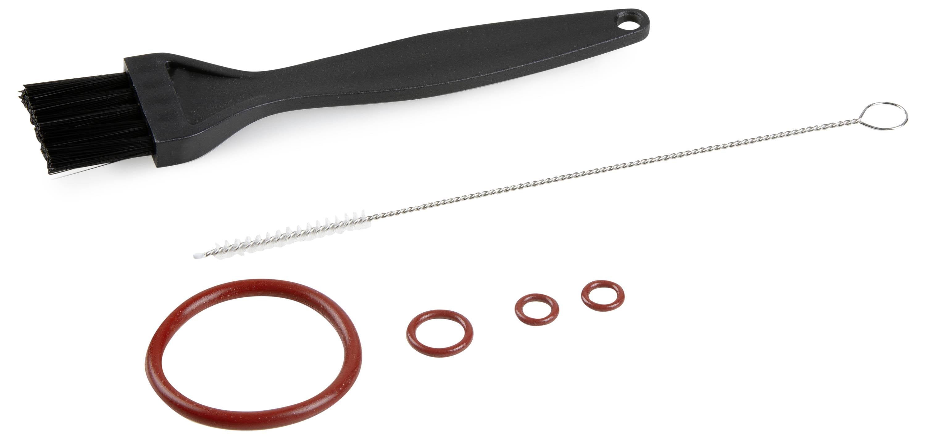 Czarny pędzel, cienka szczoteczka do czyszczenia oraz cztery czerwone pierścienie uszczelniające o różnych rozmiarach leżą na białej powierzchni.