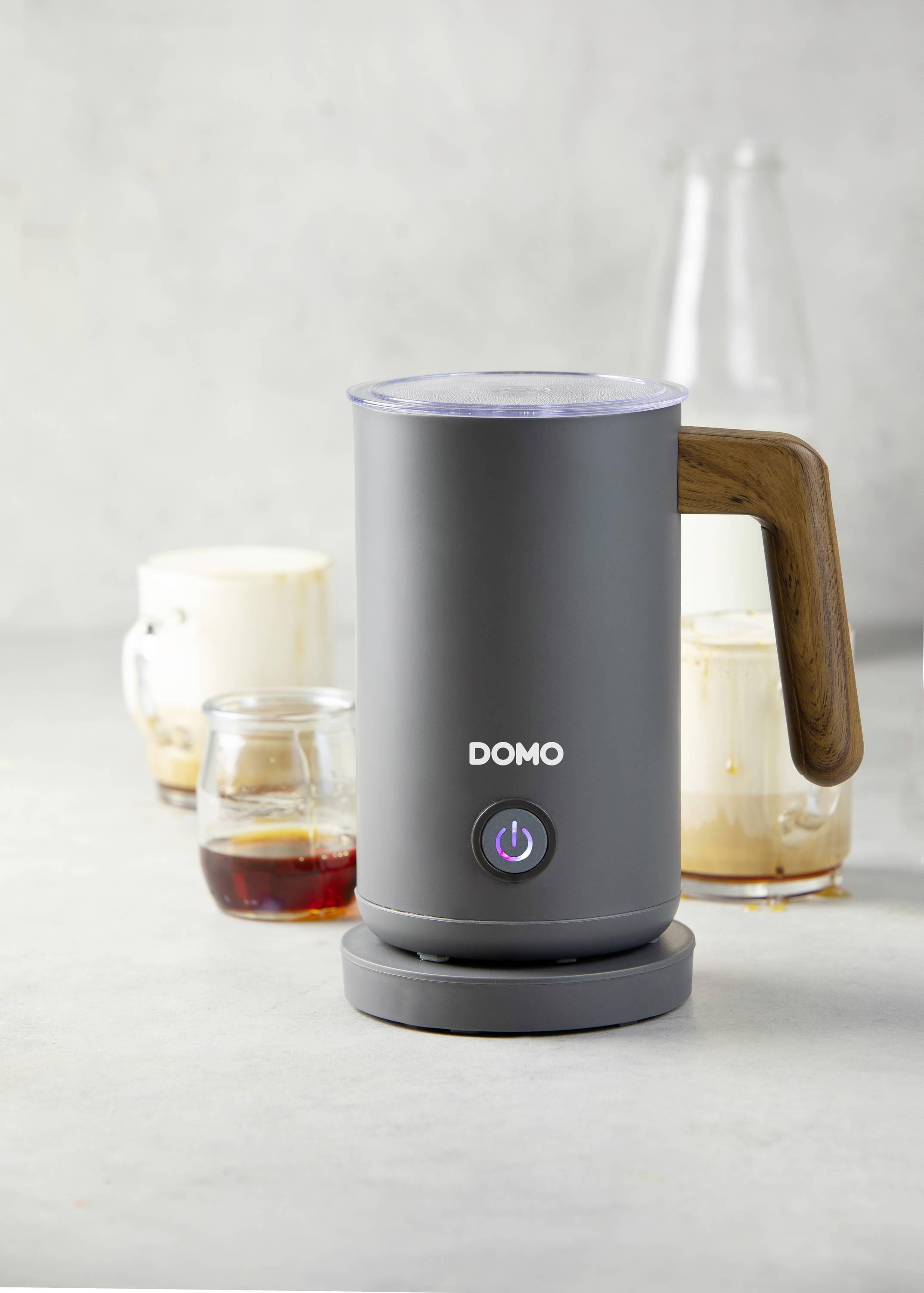 Elektryczny spieniacz do mleka z drewnianą rączką, otoczony szklankami kawy i mlecznej pianki. Idealny do przygotowywania kawy.