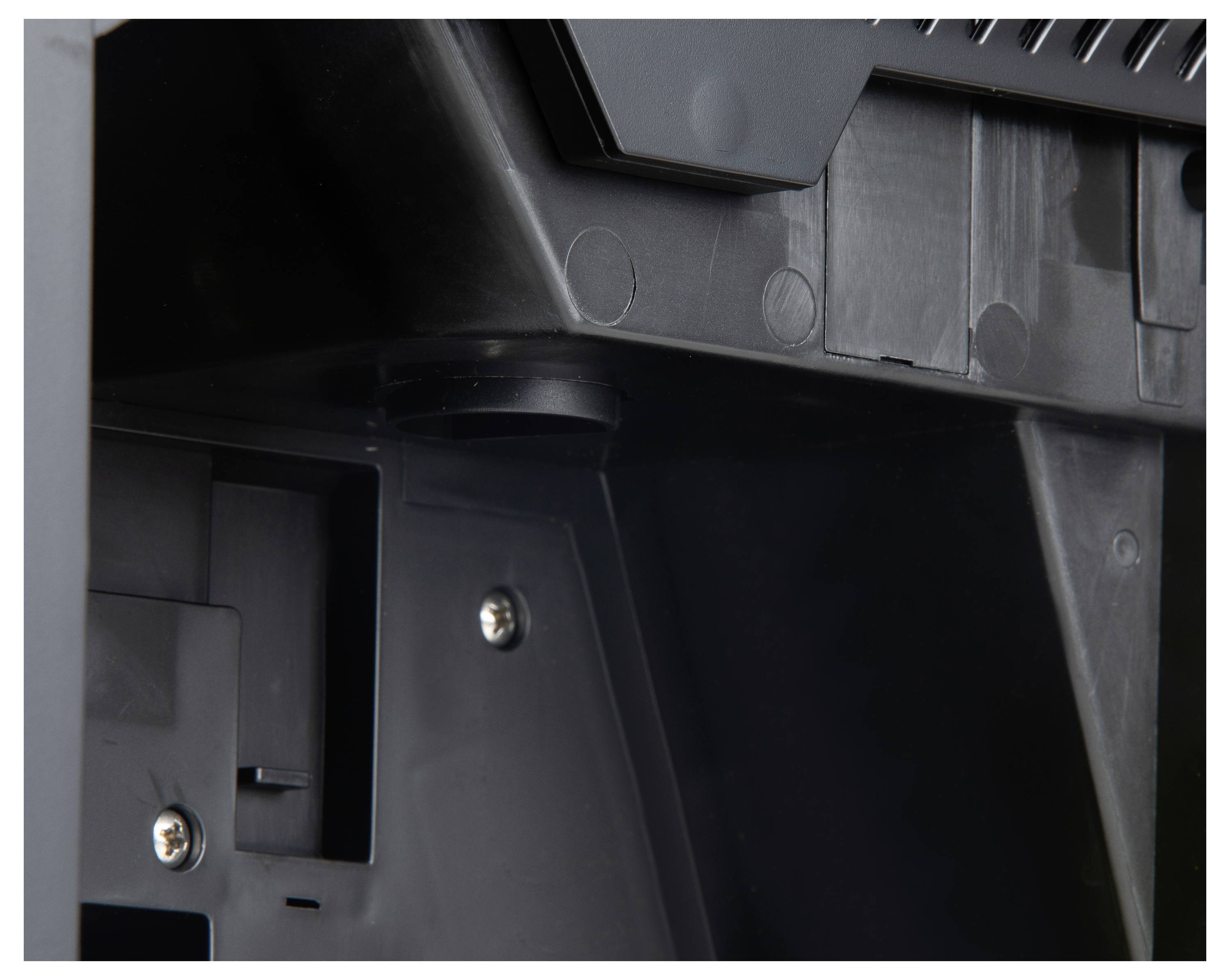 Zbliżenie fragmentu czarnej obudowy z tworzywa sztucznego z widocznymi śrubami i współpracującymi elementami, prawdopodobnie części urządzenia elektronicznego.