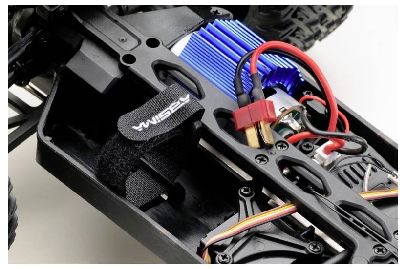 Szczegółowy widok podwozia samochodu sterowanego zdalnie, prezentujący komponenty elektroniczne i okablowanie, w tym niebieski radiator i kable zasilające.