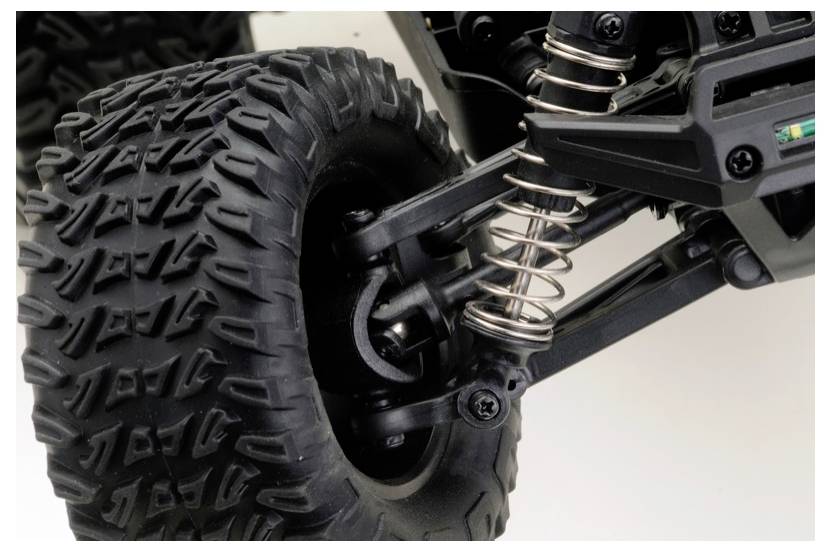 Zbliżenie na koło pojazdu terenowego, pokazujące dużą oponę z głębokim bieżnikiem i widoczne sprężyny zawieszenia, wskazujące na zdolność do jazdy w trudnym terenie.