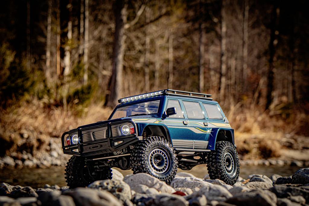 Miniaturowy samochód terenowy stoi na skałach na tle rozmytego krajobrazu przyrody.