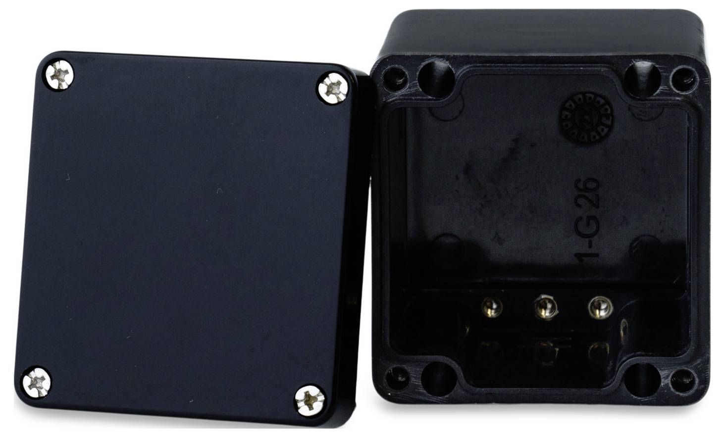 Czarne puszki rozgałęźne z tworzywa sztucznego, jedna zamknięta, druga otwarta, prezentujące wnętrze i otwory na śruby.