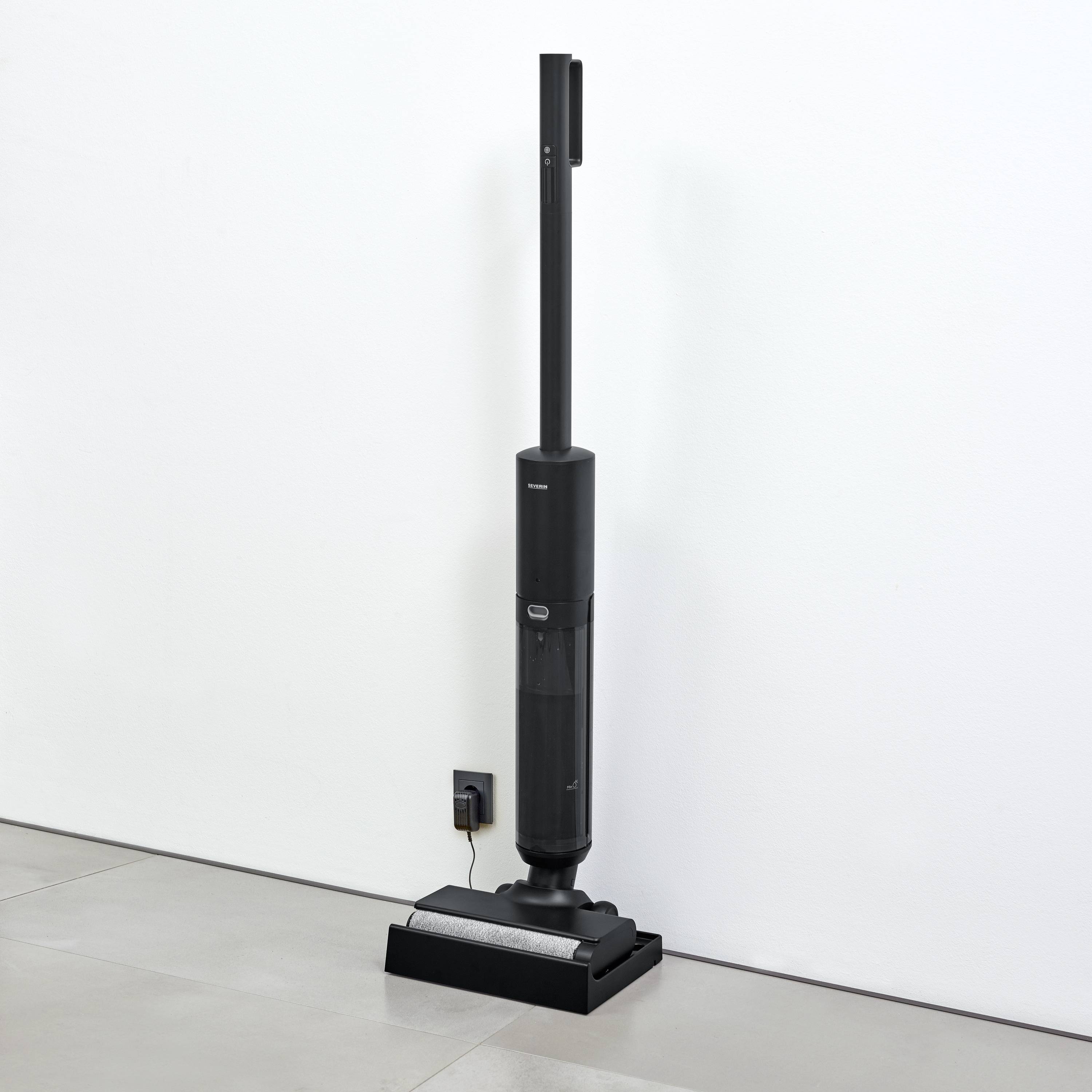 Czarny bezprzewodowy odkurzacz stoi w stacji ładującej obok białej ściany na jasnoszarej podłodze.