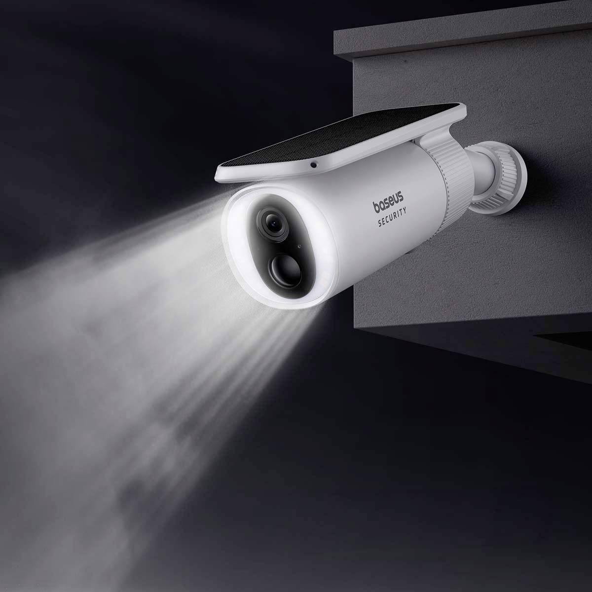 'Biała kamera monitorująca z modułem solarnym i czujnikiem ruchu, zamontowana na ścianie, wysyłająca światło w ciemne otoczenie.'