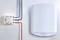 Białe urządzenie elektryczne zamontowane na ścianie obok małego pudełka z kolorowymi przewodami; prawdopodobnie element systemu grzewczego lub energetycznego.