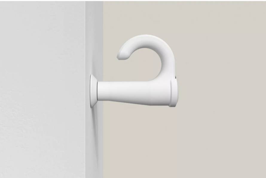 Biały uchwyt zamocowany jest na ścianie, przy czym hak skierowany jest w górę, na beżowym tle.